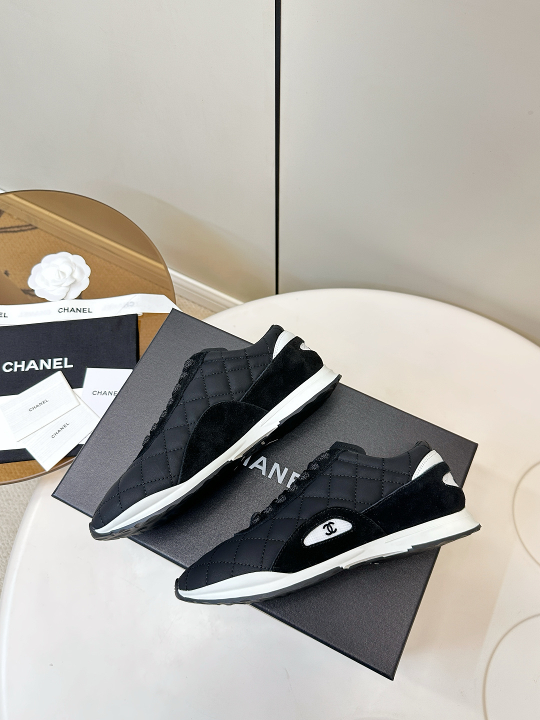 A pair of black Chanel quilted fabric sneakers with white soles and CC logo sitting on a black branded box. - Hình 9
