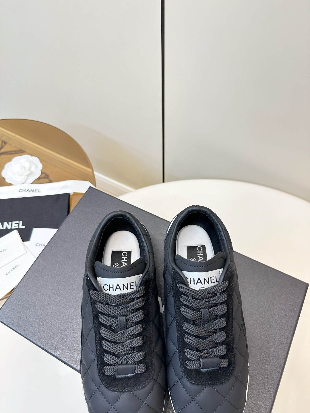 A pair of black Chanel quilted fabric sneakers with white soles and CC logo sitting on a black branded box. - Hình 8