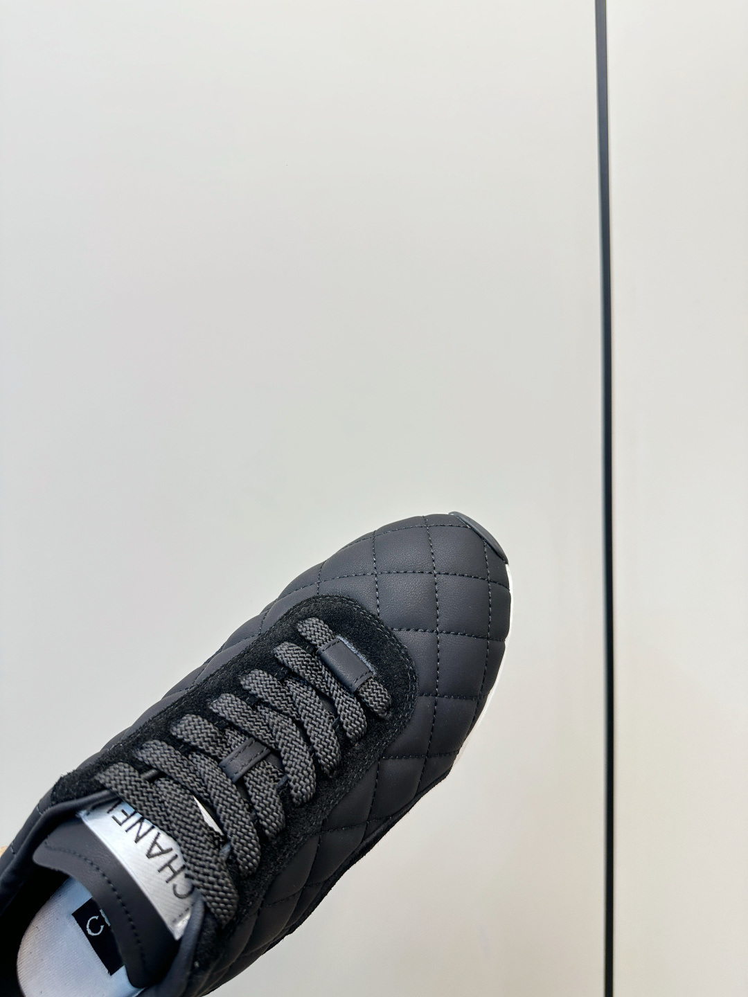 A pair of black Chanel quilted fabric sneakers with white soles and CC logo sitting on a black branded box. - Hình 7