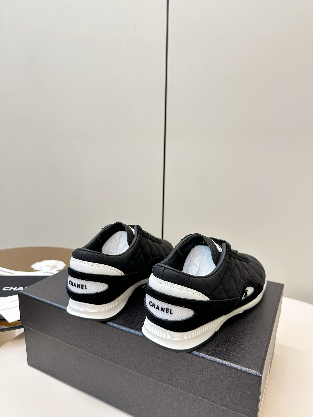 A pair of black Chanel quilted fabric sneakers with white soles and CC logo sitting on a black branded box. - Hình 4