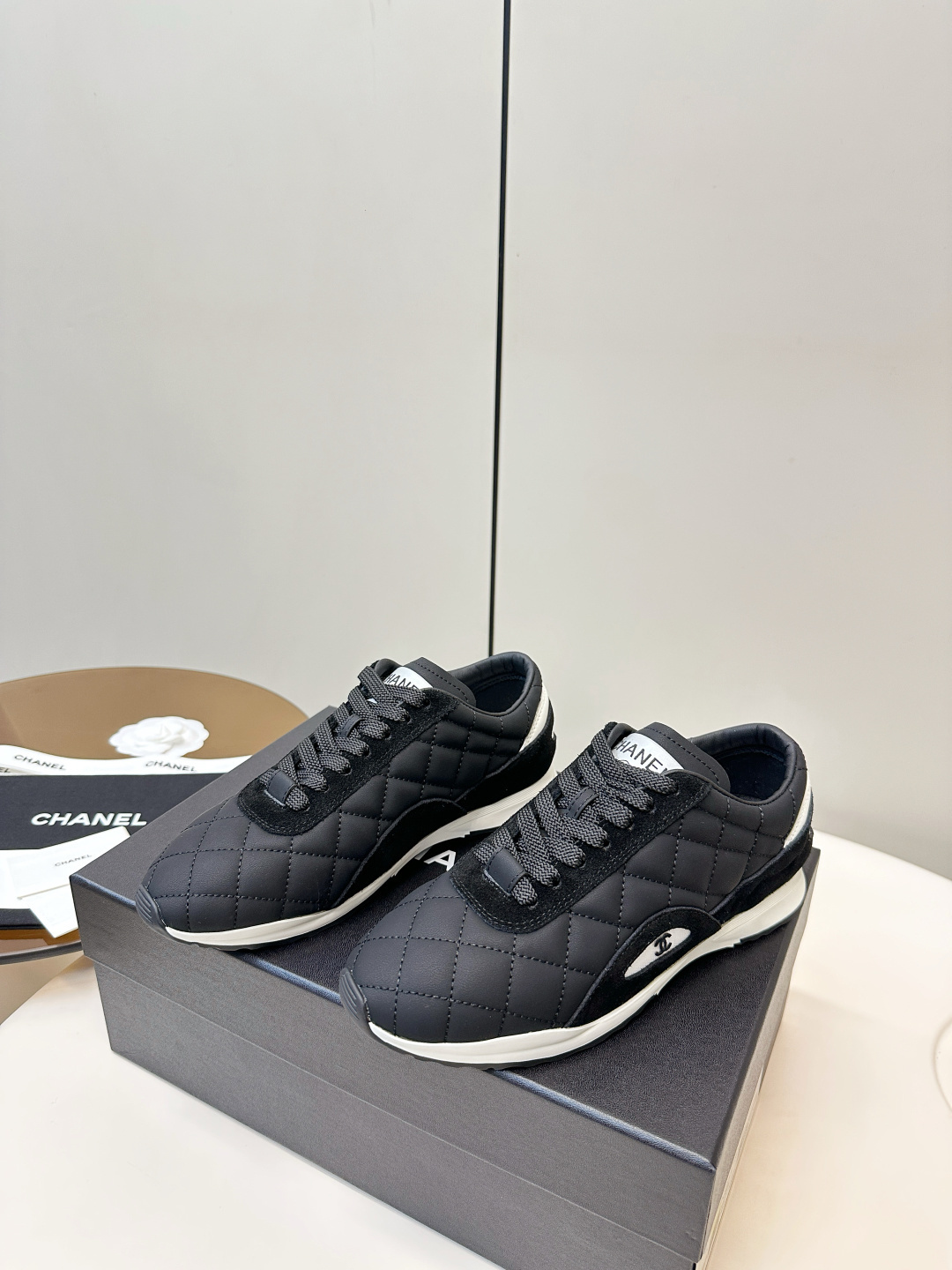 A pair of black Chanel quilted fabric sneakers with white soles and CC logo sitting on a black branded box. - Hình 3