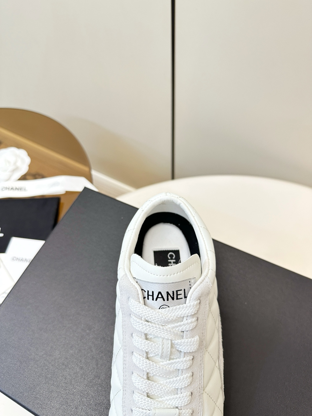 A pair of luxury white Chanel sneakers with a quilted pattern and CC logo resting on a black Chanel shoe box. - Hình 8