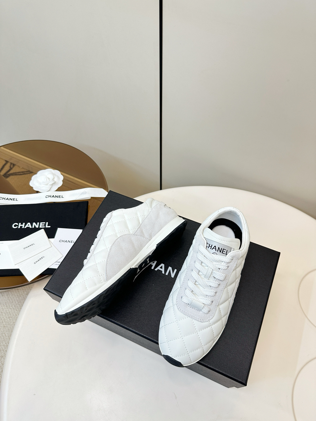 A pair of luxury white Chanel sneakers with a quilted pattern and CC logo resting on a black Chanel shoe box. - Hình 5