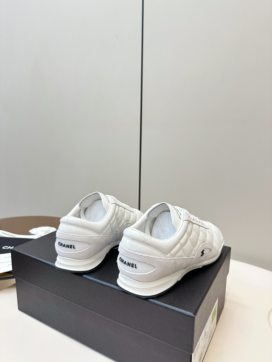 A pair of luxury white Chanel sneakers with a quilted pattern and CC logo resting on a black Chanel shoe box. - Hình 4