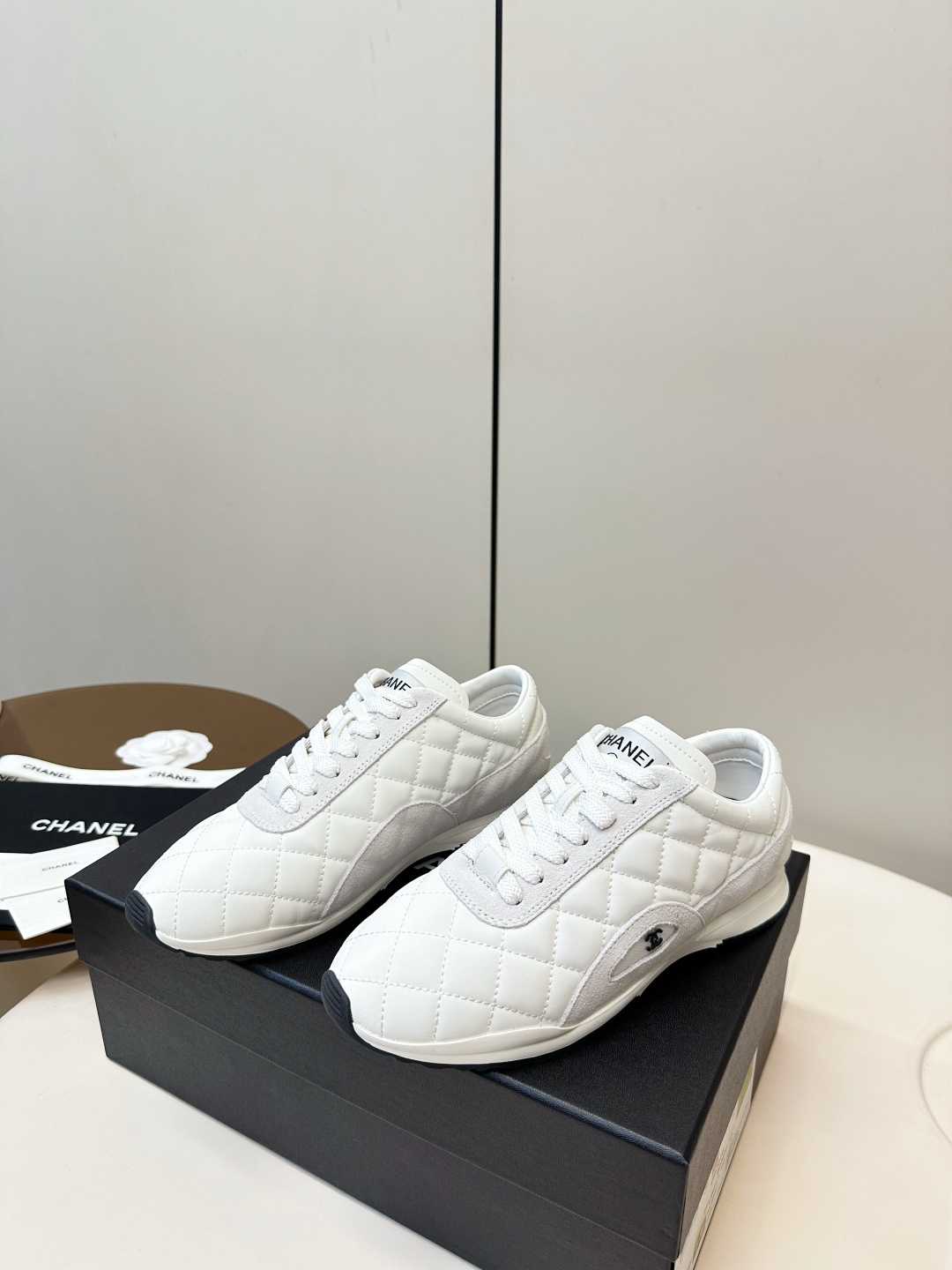 A pair of luxury white Chanel sneakers with a quilted pattern and CC logo resting on a black Chanel shoe box. - Hình 3