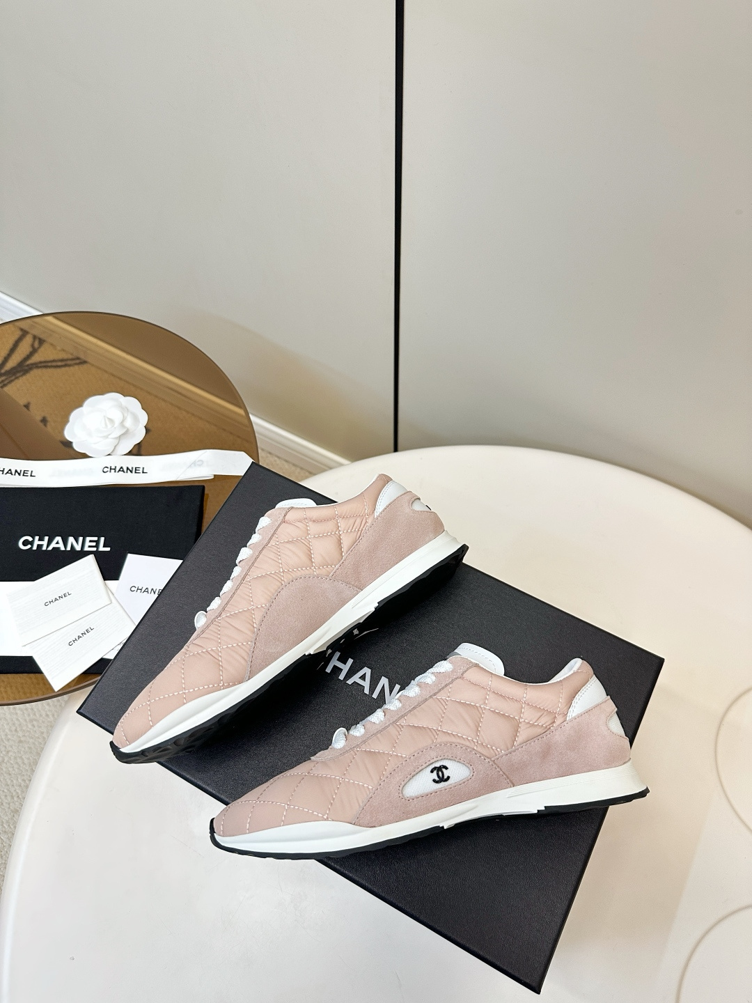 A pair of light pink Chanel quilted sneakers with white laces resting on a black designer box. - Hình 9
