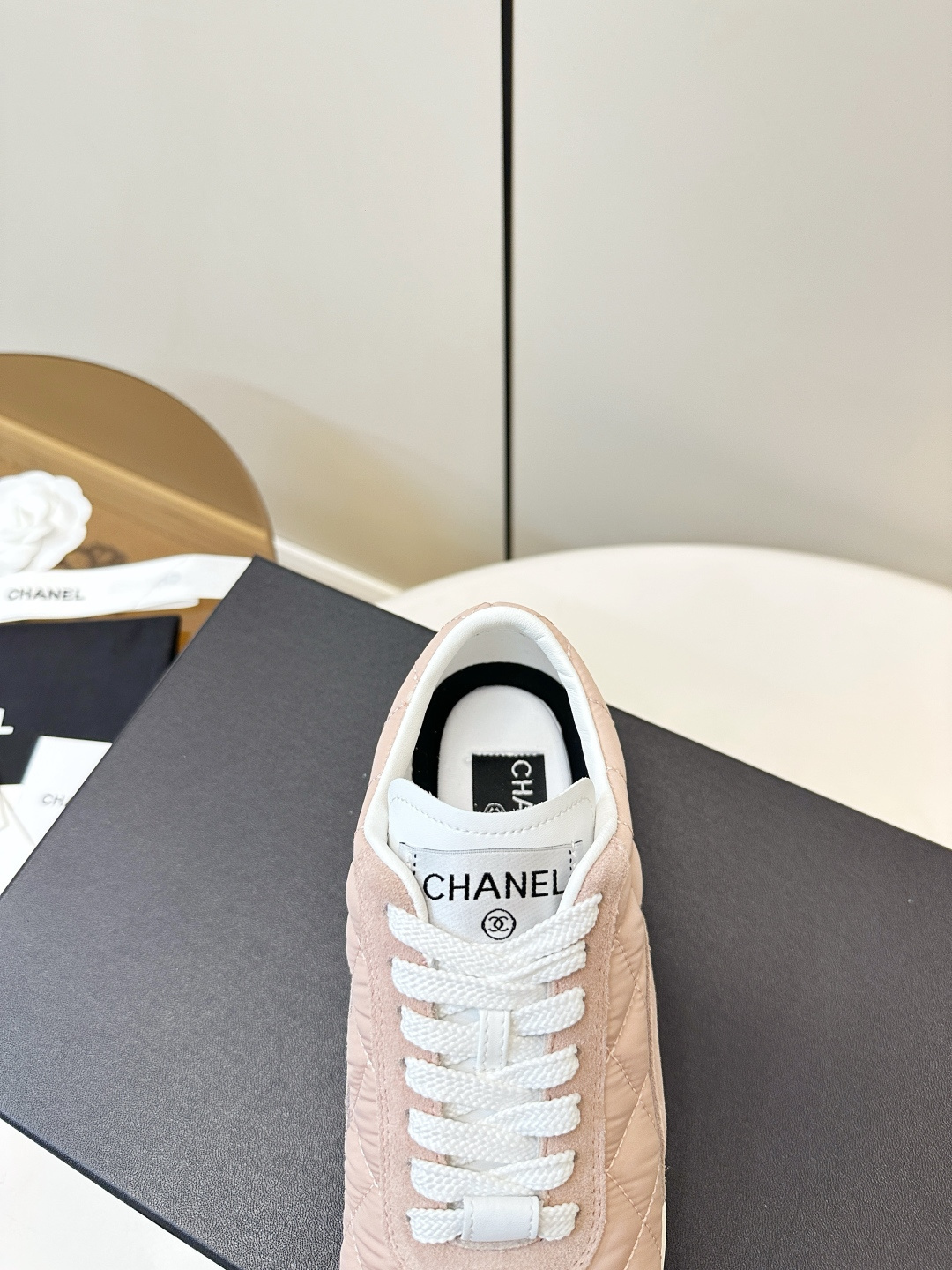 A pair of light pink Chanel quilted sneakers with white laces resting on a black designer box. - Hình 8