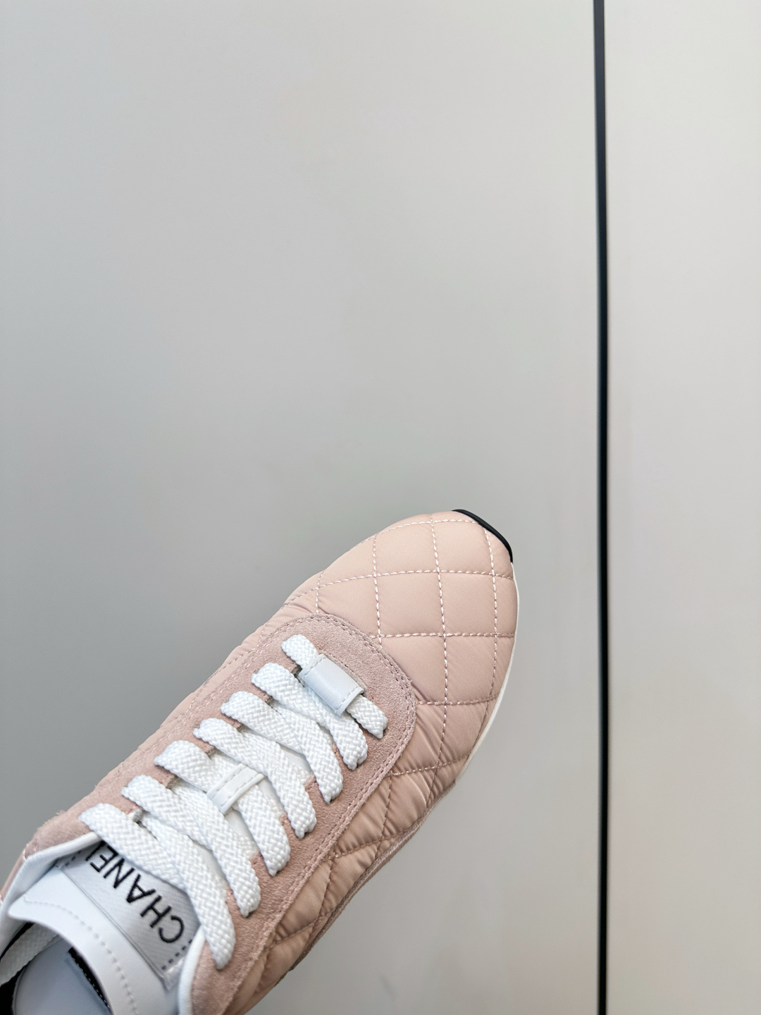 A pair of light pink Chanel quilted sneakers with white laces resting on a black designer box. - Hình 7