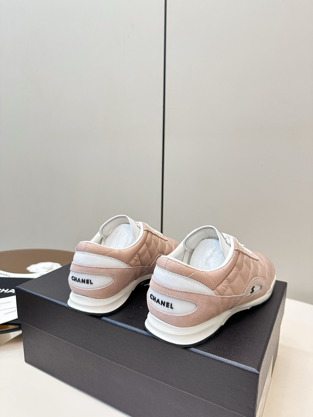 A pair of light pink Chanel quilted sneakers with white laces resting on a black designer box. - Hình 4