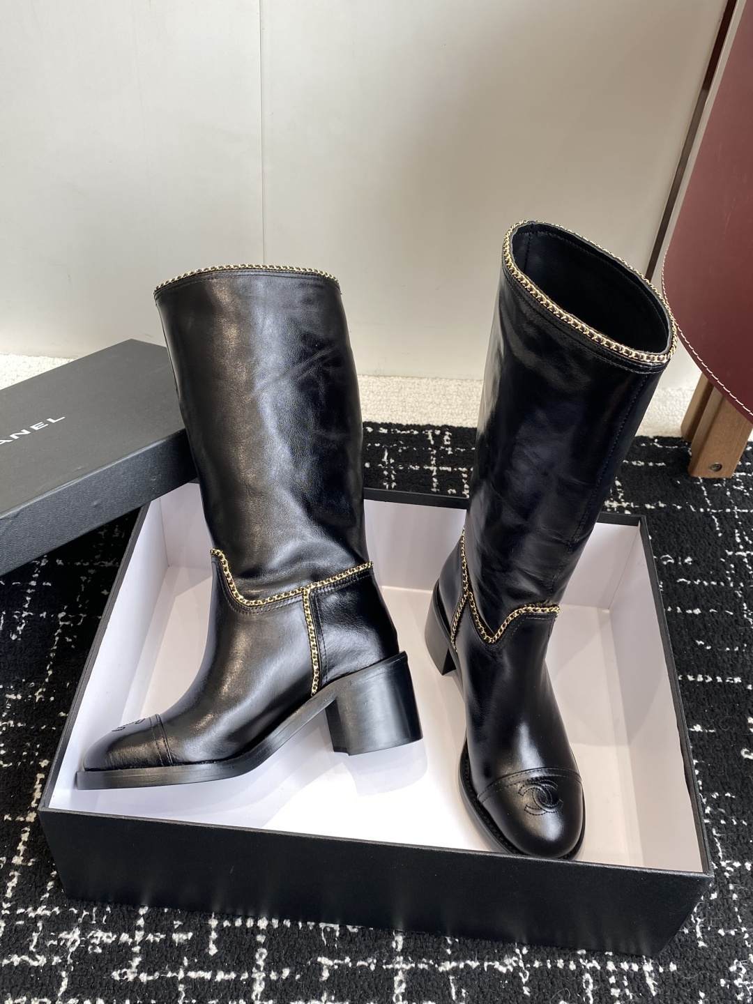 Pair of black Chanel leather knee-high boots with gold chain trim and embossed CC logo on the toe cap. - Hình 5