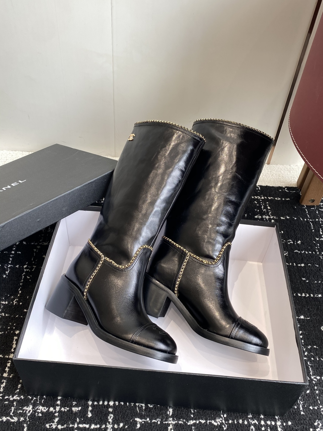 Pair of black Chanel leather knee-high boots with gold chain trim and embossed CC logo on the toe cap. - Hình 4