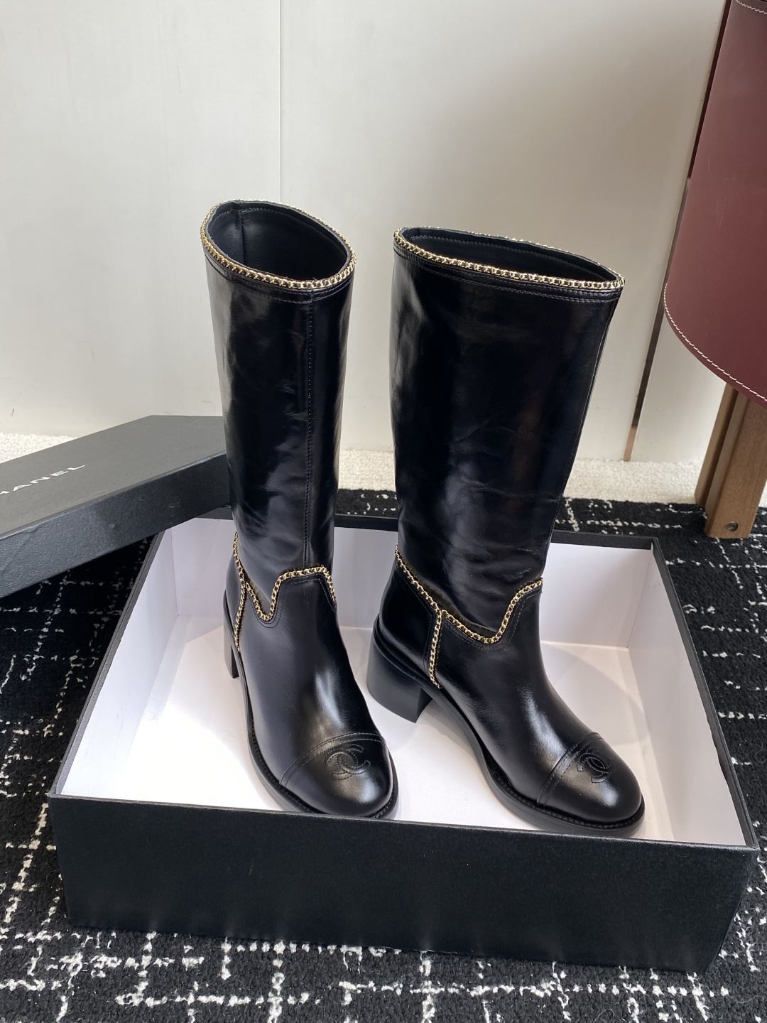 Pair of black Chanel leather knee-high boots with gold chain trim and embossed CC logo on the toe cap. - Hình 3