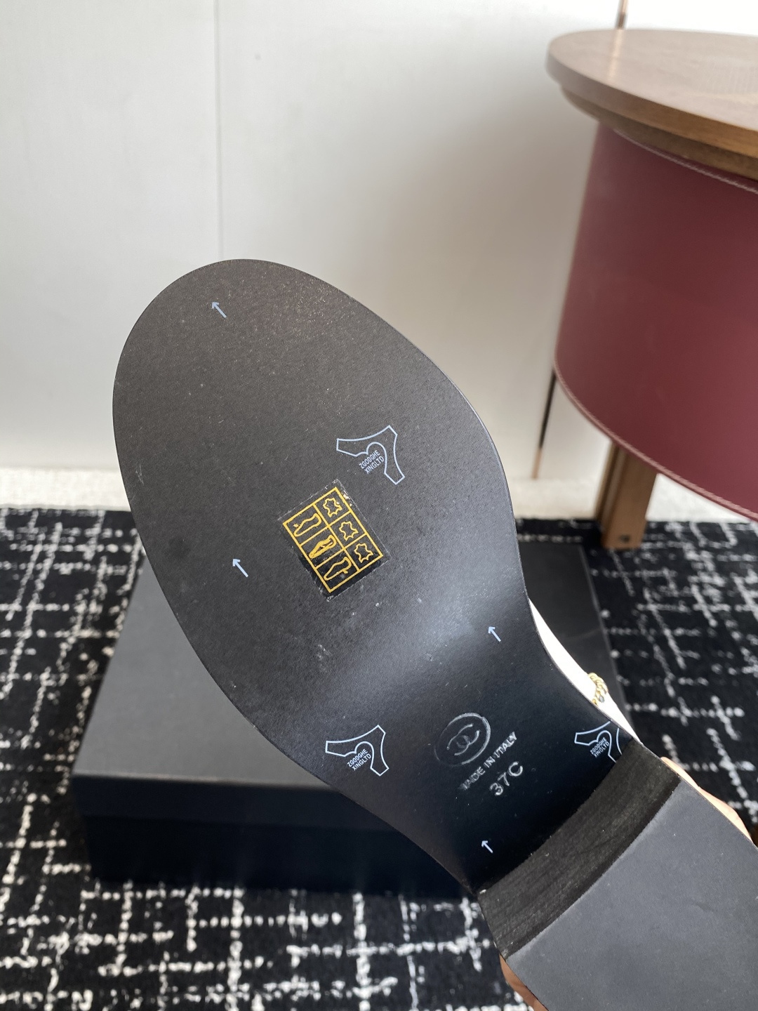 Pair of luxury white and black two-tone knee-high boots with gold chain trim and block heels on a black display box. - Hình 9