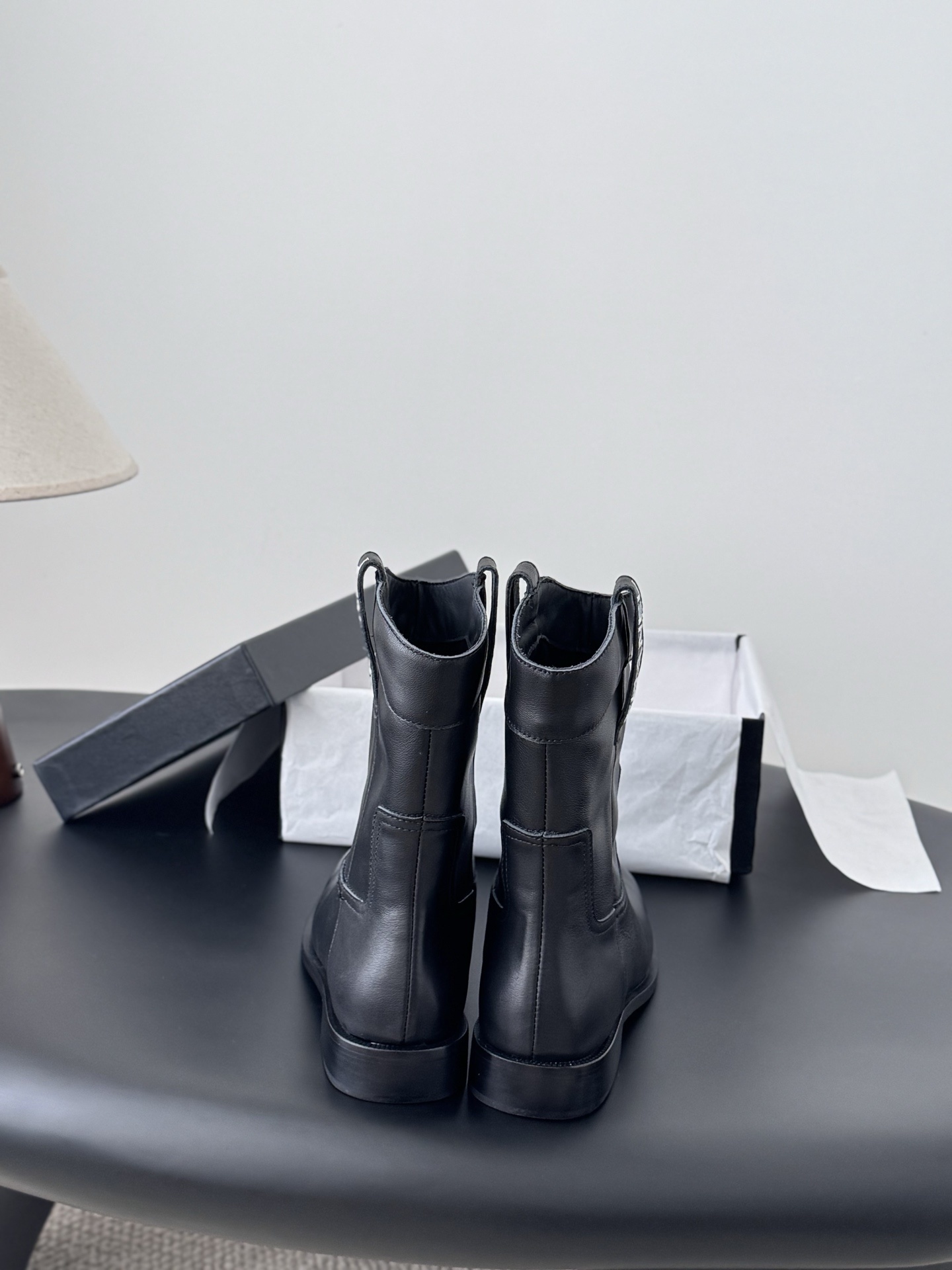A pair of Chanel black leather mid-calf boots with silver logo hardware on the pull tabs, displayed next to a Chanel designer box. - Hình 6