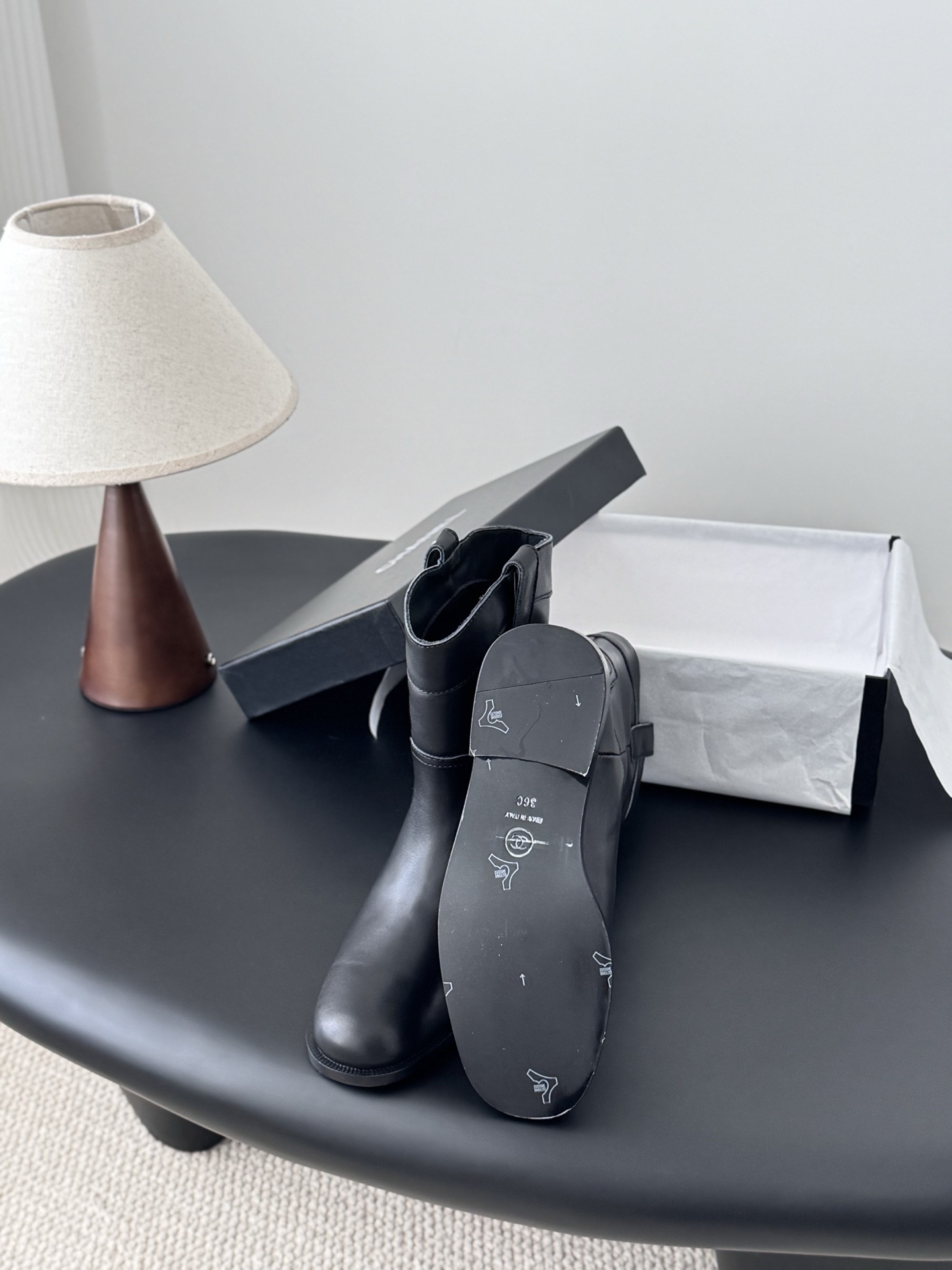 A pair of Chanel black leather mid-calf boots with silver logo hardware on the pull tabs, displayed next to a Chanel designer box. - Hình 4