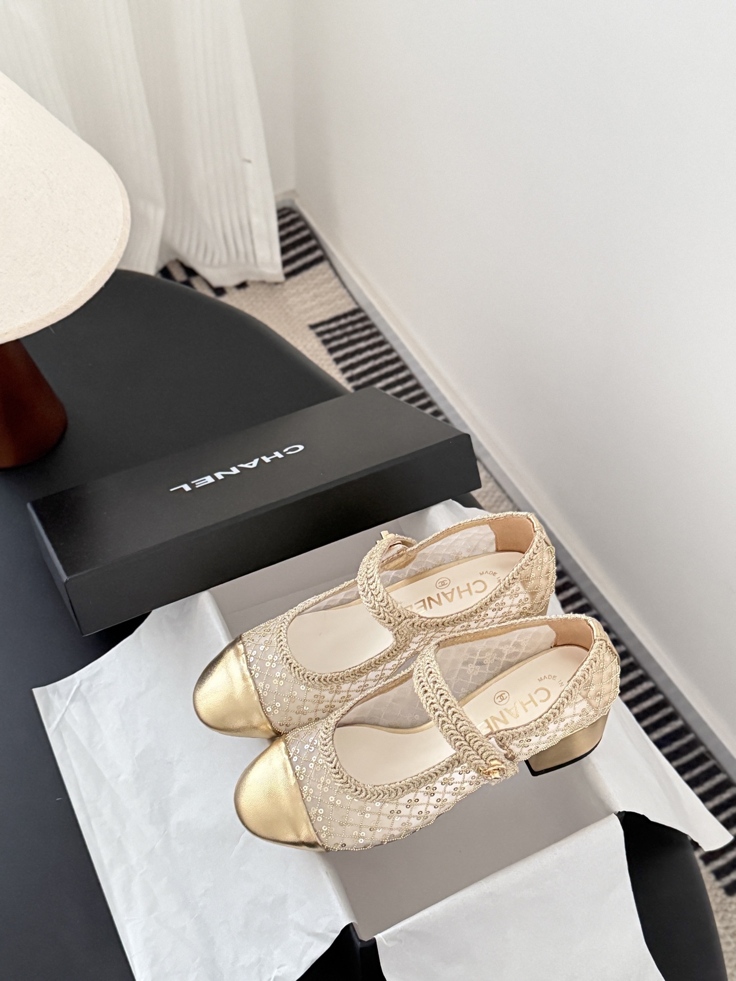A pair of Chanel gold sequin mesh Mary Jane heels with a gold leather cap toe and block heel on a black table next to a Chanel box. - Hình 9