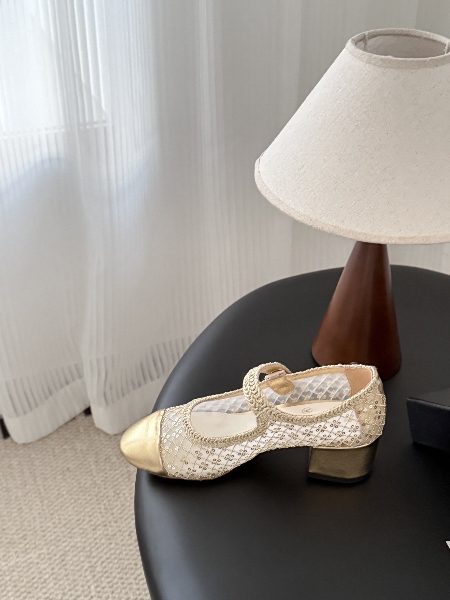 A pair of Chanel gold sequin mesh Mary Jane heels with a gold leather cap toe and block heel on a black table next to a Chanel box. - Hình 6