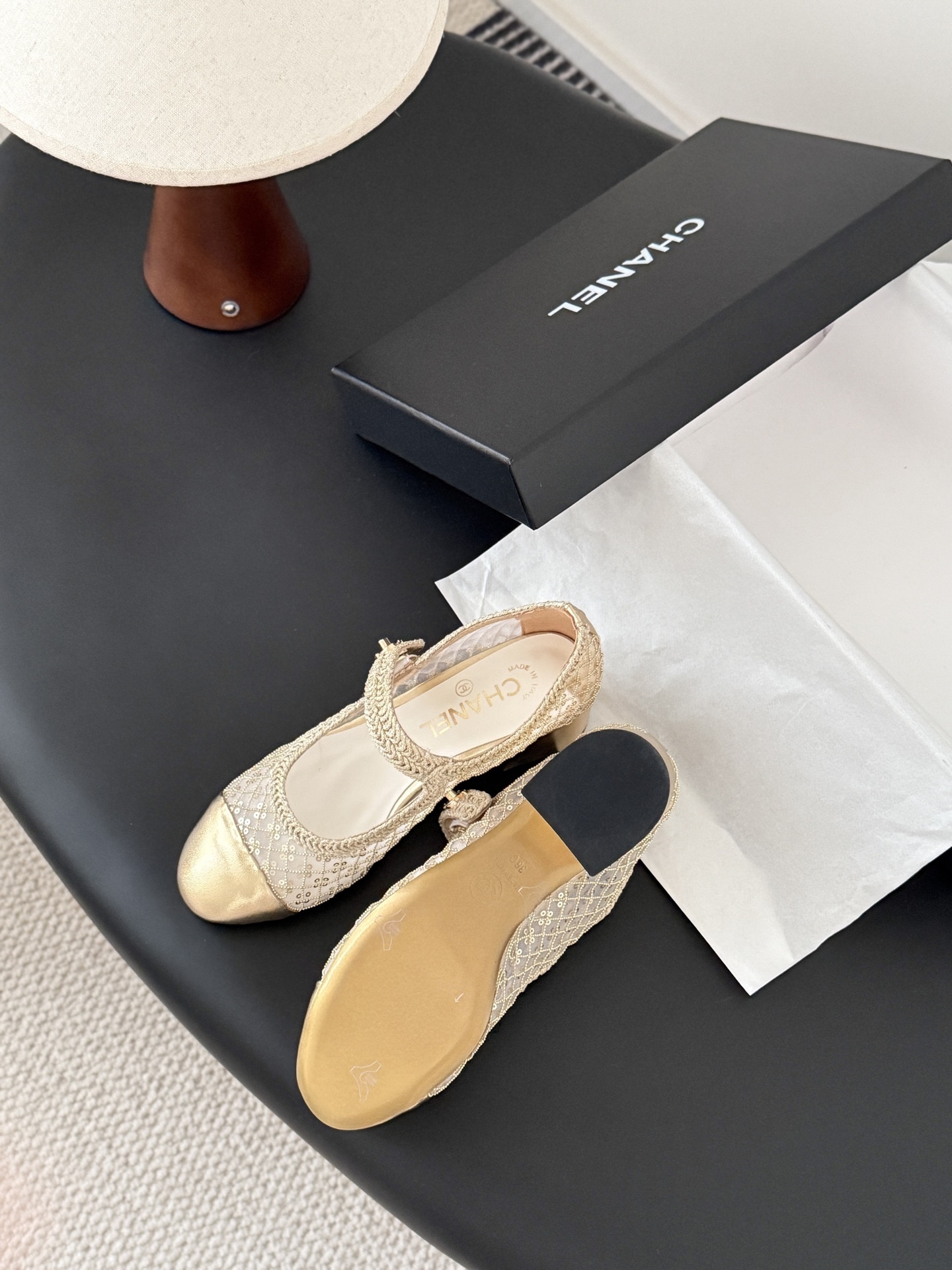 A pair of Chanel gold sequin mesh Mary Jane heels with a gold leather cap toe and block heel on a black table next to a Chanel box. - Hình 5