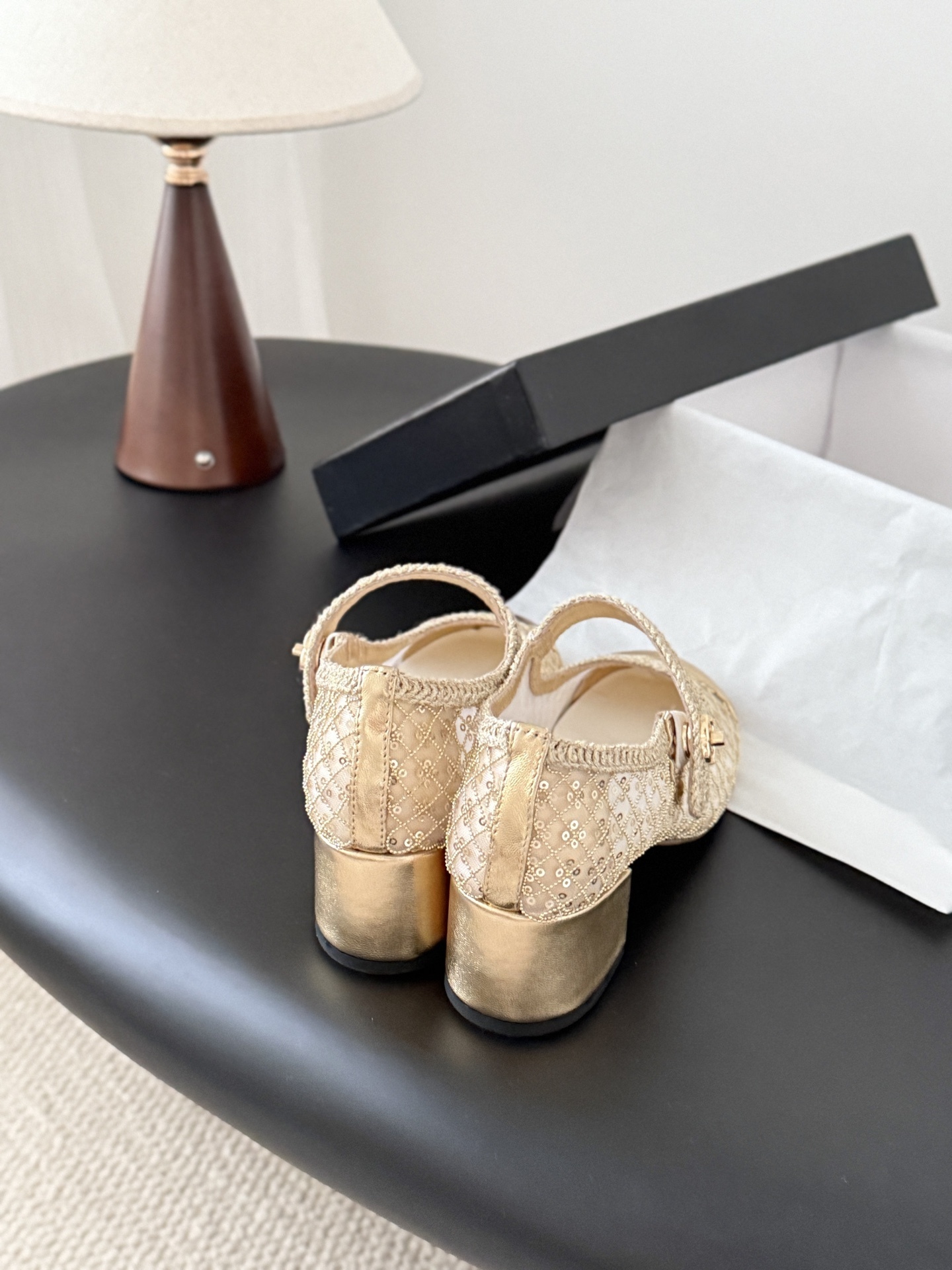 A pair of Chanel gold sequin mesh Mary Jane heels with a gold leather cap toe and block heel on a black table next to a Chanel box. - Hình 3