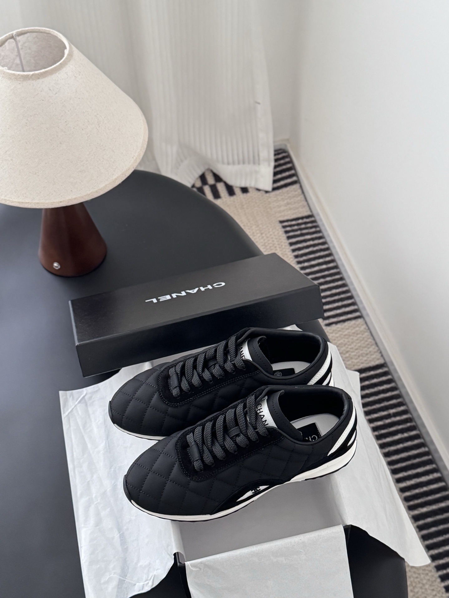 A pair of black Chanel quilted sneakers featuring the CC logo, displayed next to their original black Chanel box. - Hình 9