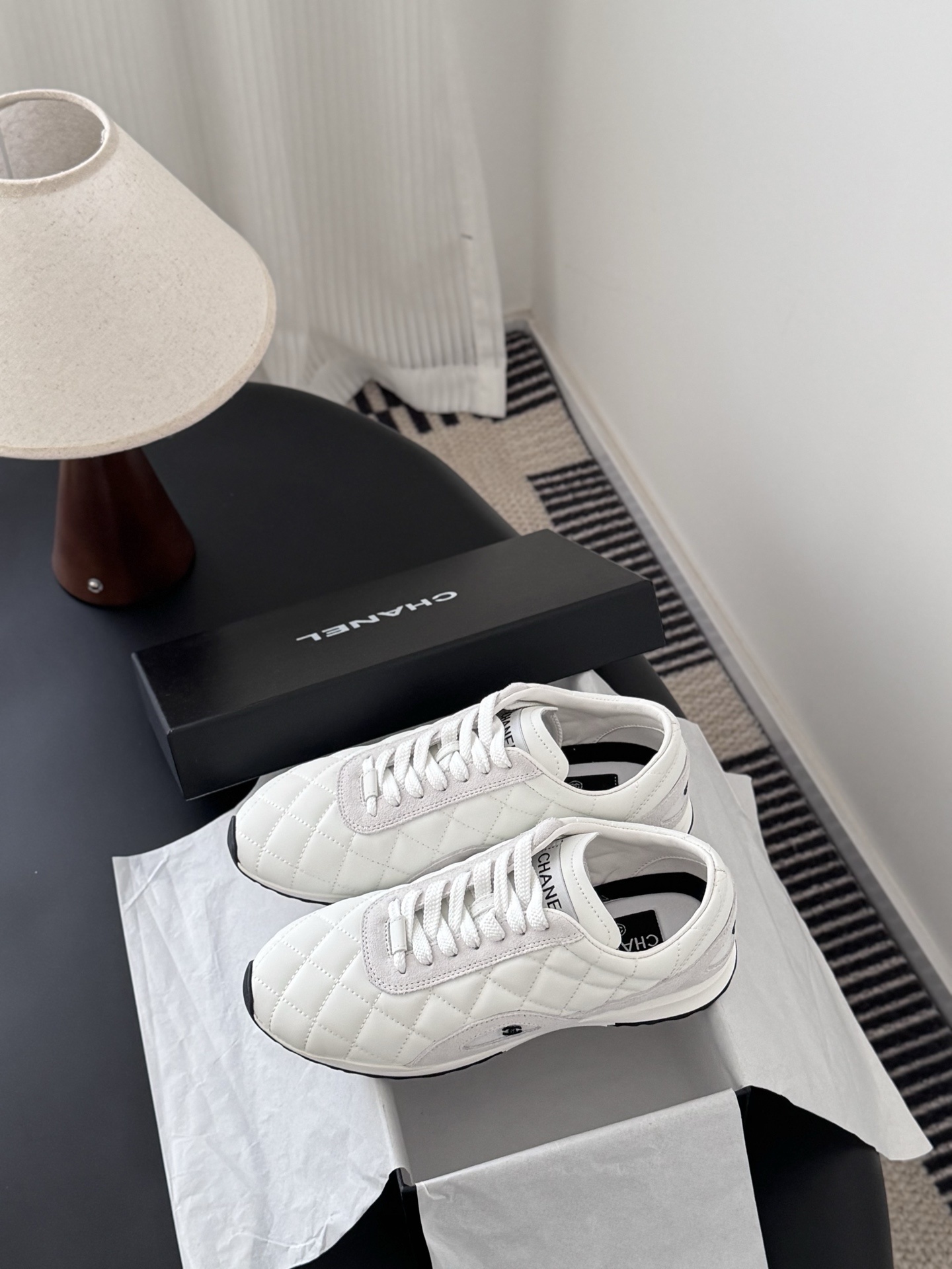 A pair of white Chanel quilted leather sneakers with suede accents next to an original black Chanel shoe box. - Hình 9