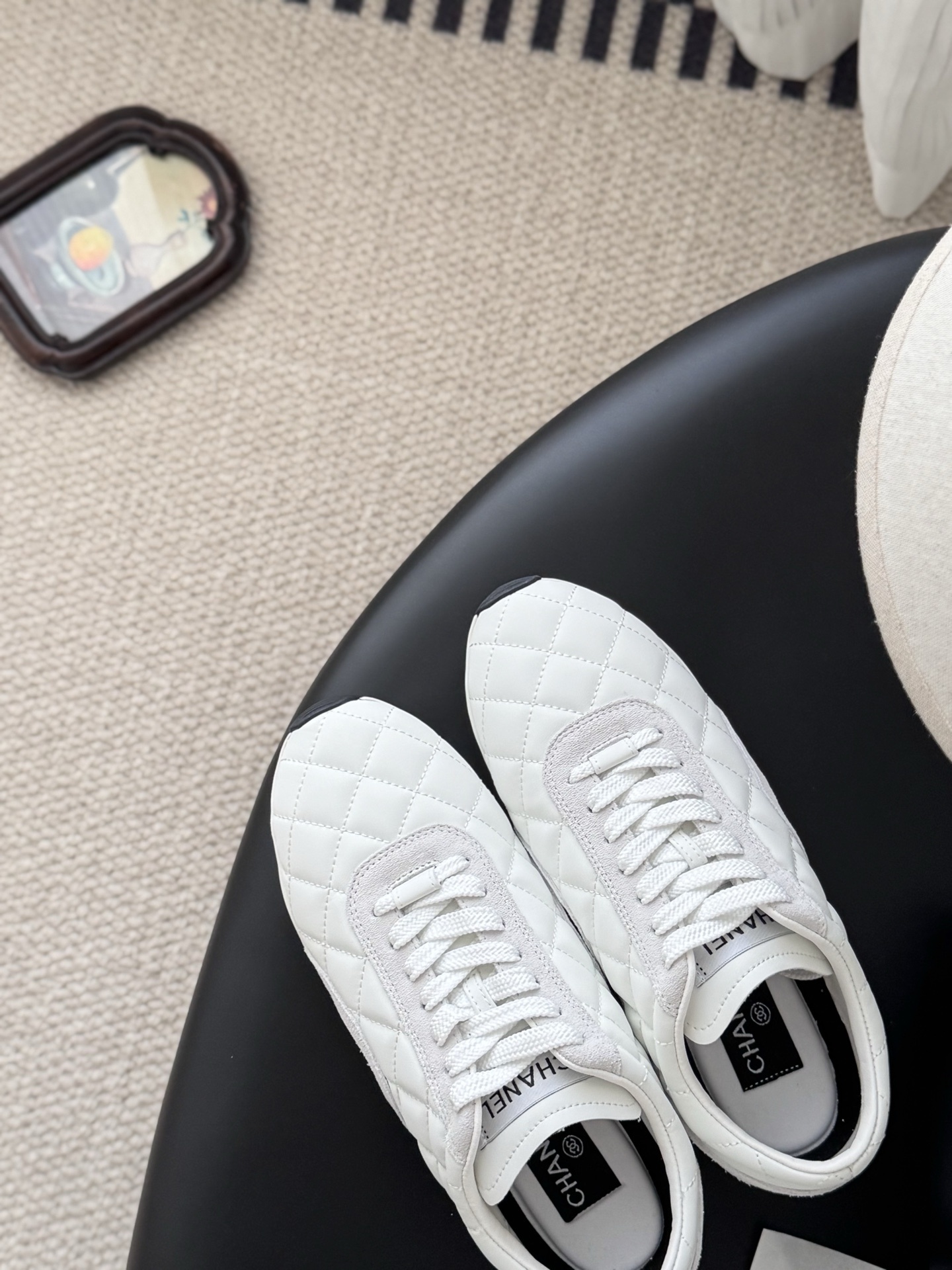 A pair of white Chanel quilted leather sneakers with suede accents next to an original black Chanel shoe box. - Hình 7