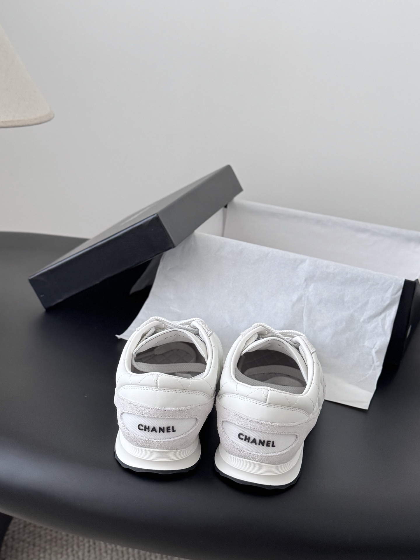 A pair of white Chanel quilted leather sneakers with suede accents next to an original black Chanel shoe box. - Hình 6