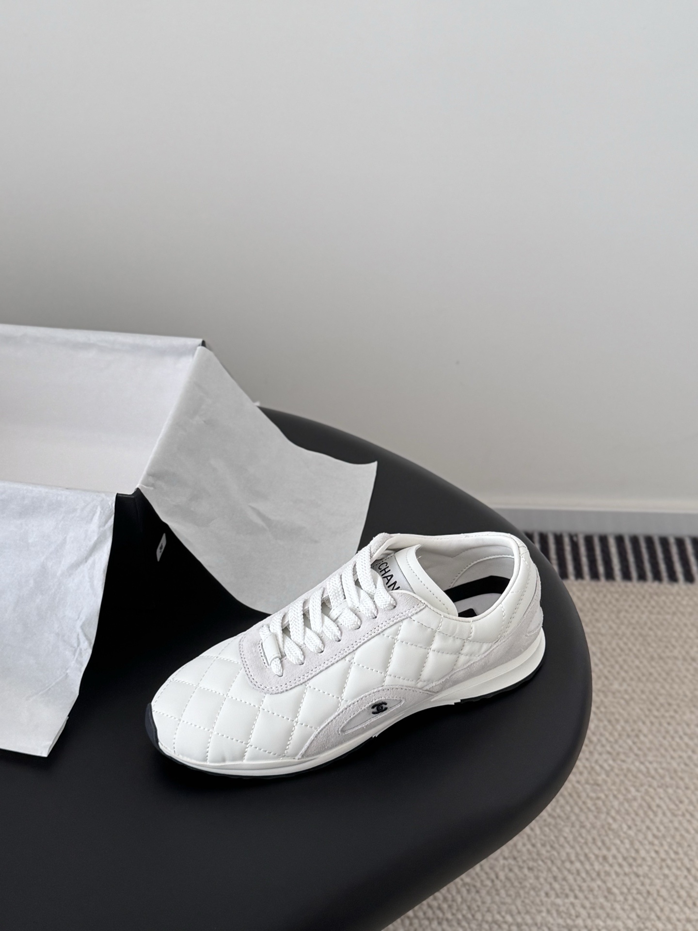 A pair of white Chanel quilted leather sneakers with suede accents next to an original black Chanel shoe box. - Hình 5