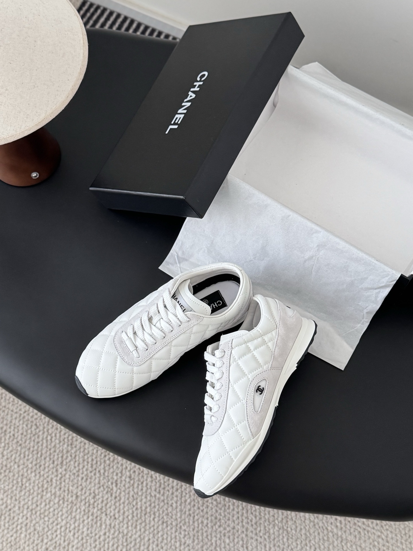 A pair of white Chanel quilted leather sneakers with suede accents next to an original black Chanel shoe box. - Hình 3