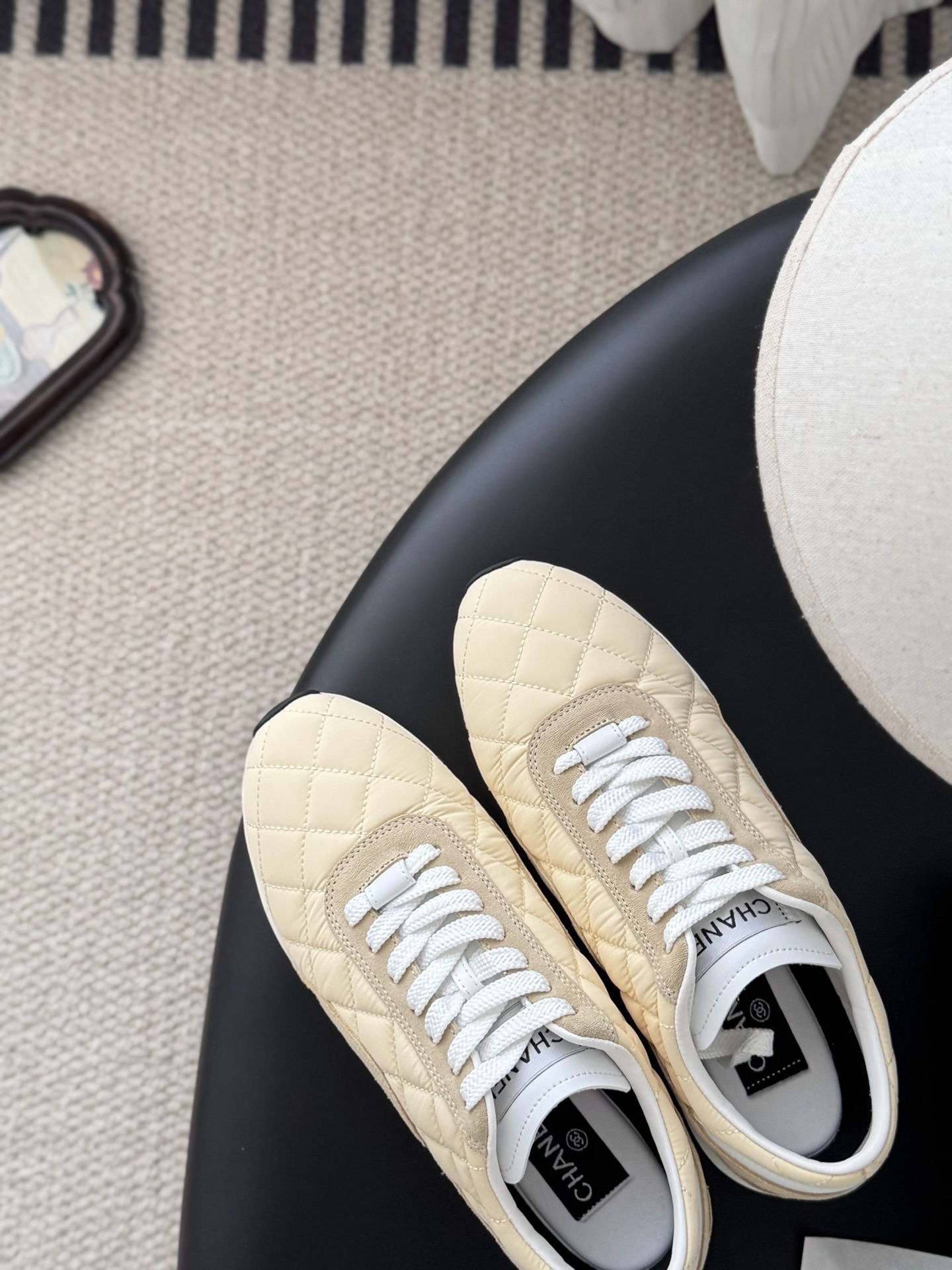 A pair of luxury Chanel sneakers in quilted pale yellow fabric with suede accents and white laces, displayed next to a black Chanel shoebox. - Hình 7