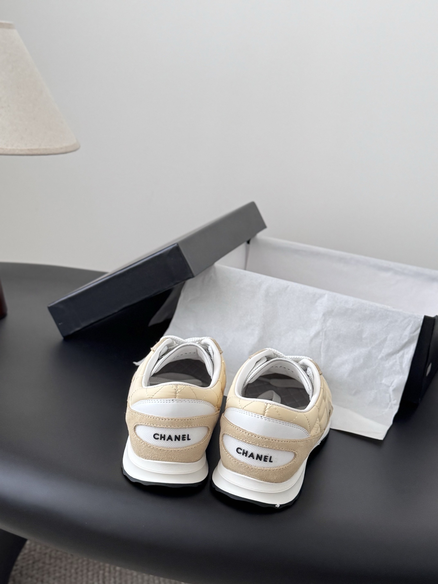 A pair of luxury Chanel sneakers in quilted pale yellow fabric with suede accents and white laces, displayed next to a black Chanel shoebox. - Hình 6