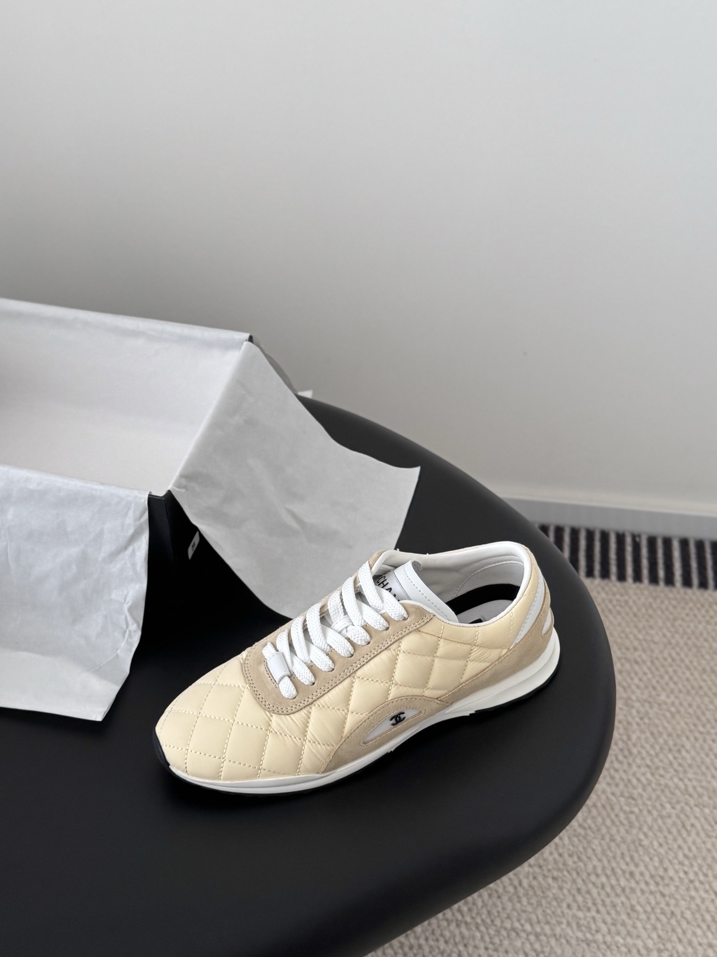 A pair of luxury Chanel sneakers in quilted pale yellow fabric with suede accents and white laces, displayed next to a black Chanel shoebox. - Hình 5
