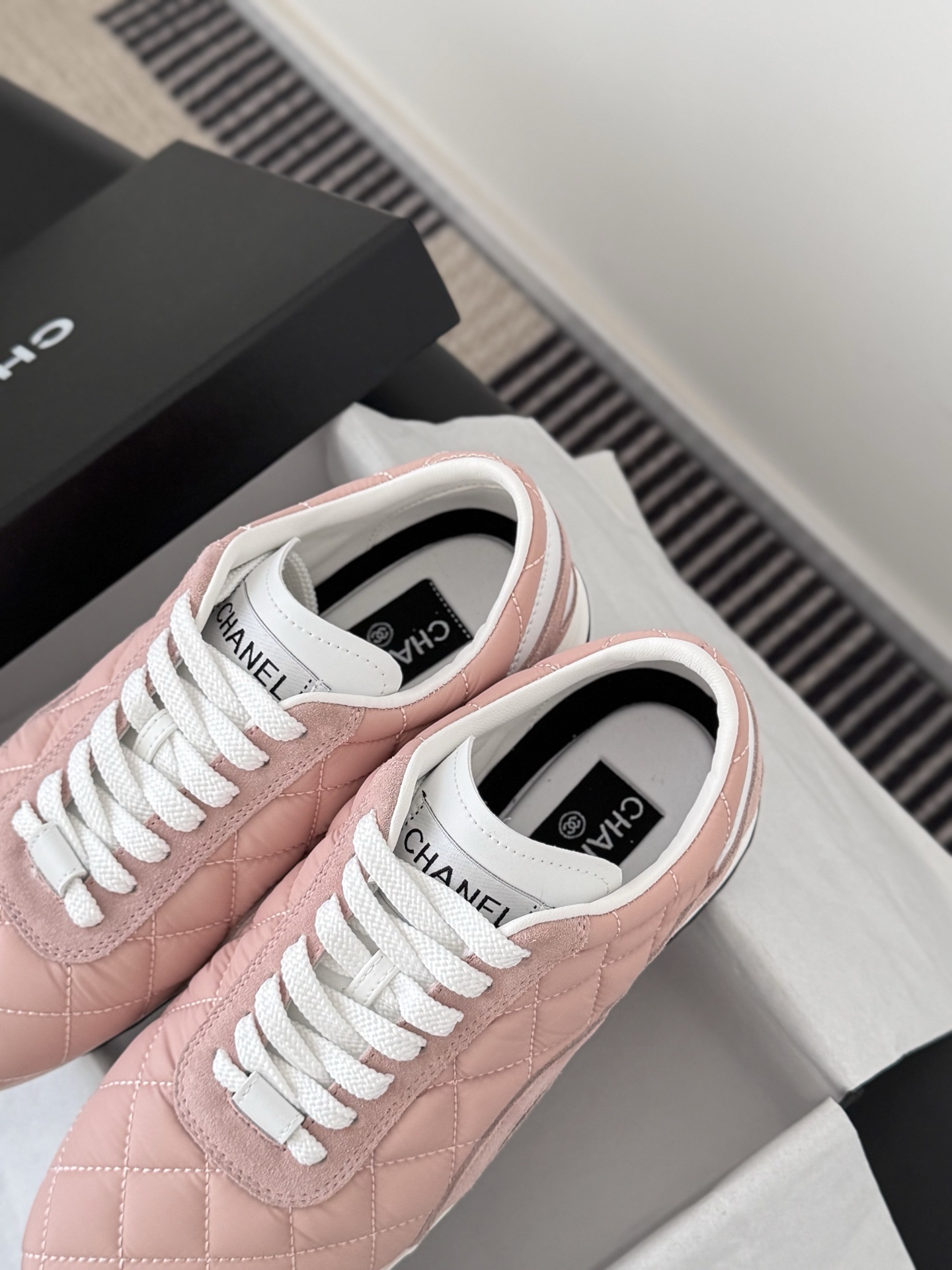 A pair of luxury pink quilted Chanel sneakers with white laces displayed next to their original black designer box. - Hình 8