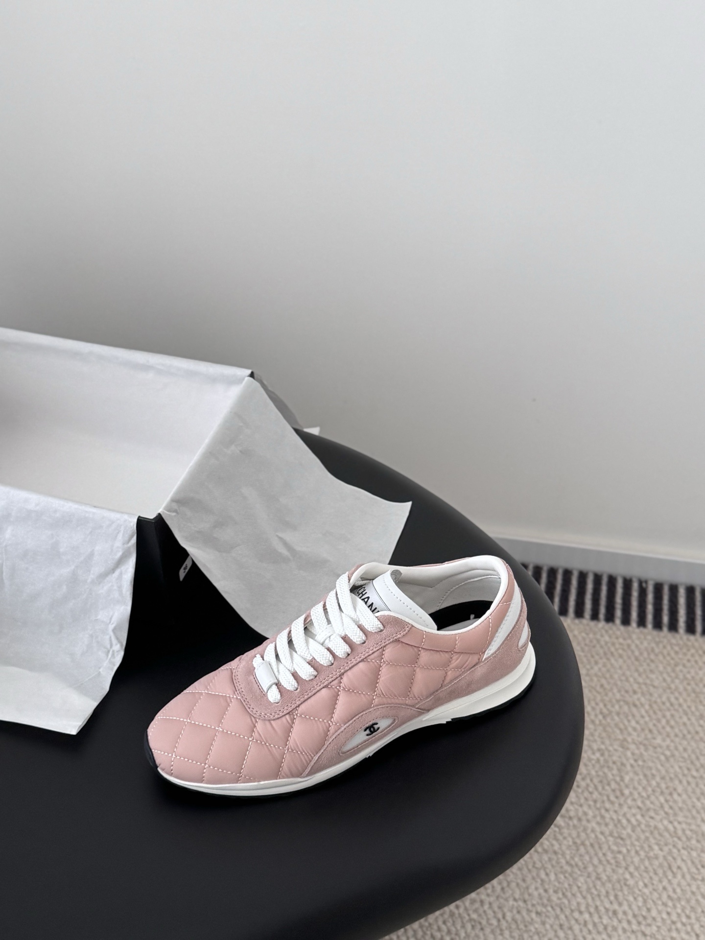 A pair of luxury pink quilted Chanel sneakers with white laces displayed next to their original black designer box. - Hình 5