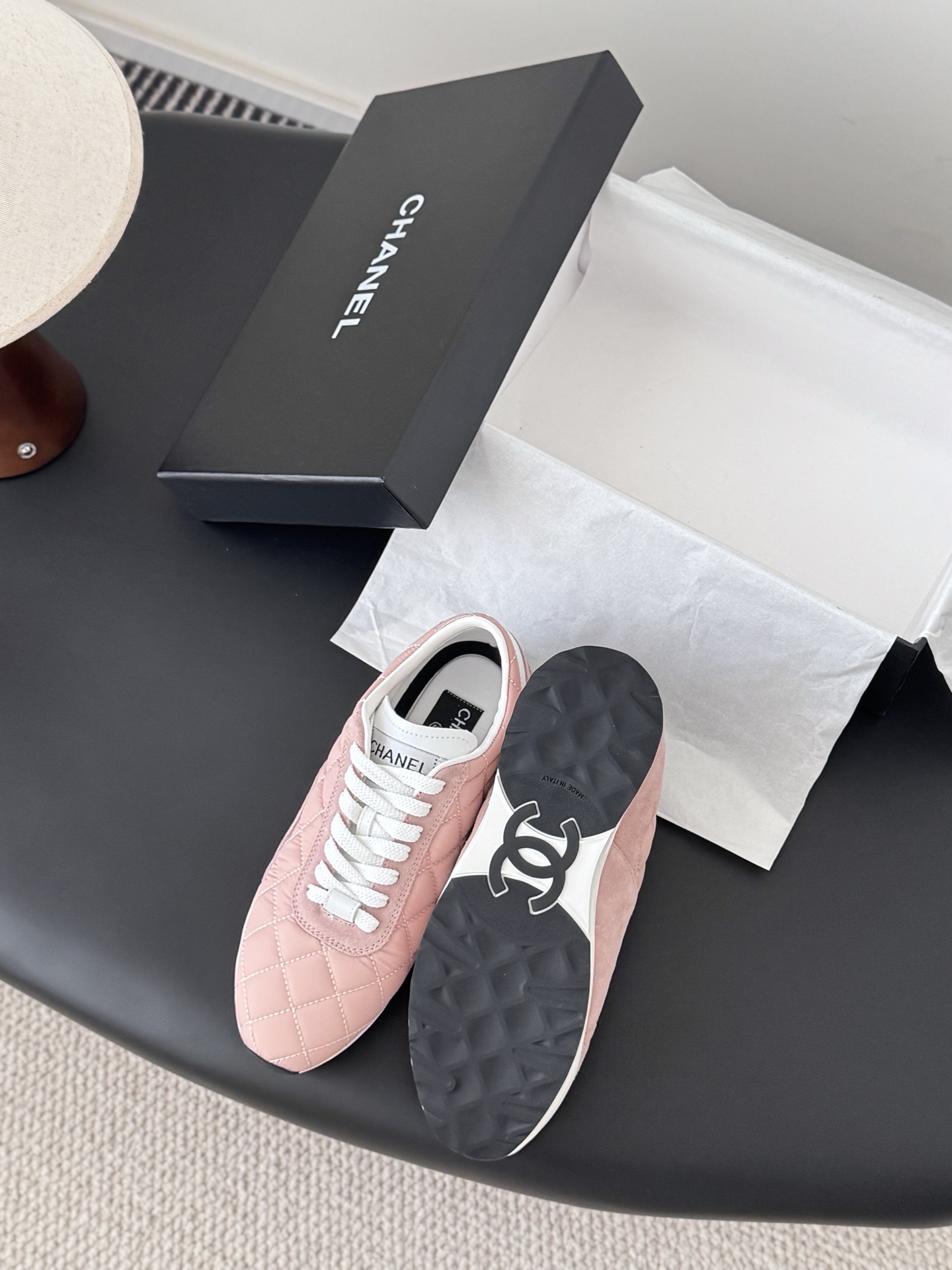 A pair of luxury pink quilted Chanel sneakers with white laces displayed next to their original black designer box. - Hình 4