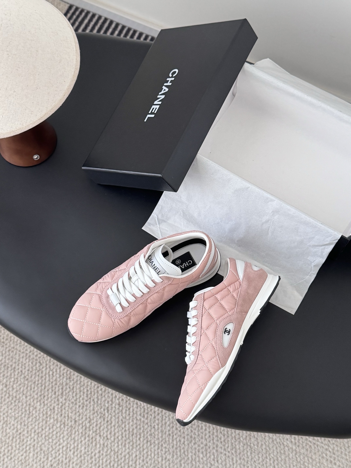 A pair of luxury pink quilted Chanel sneakers with white laces displayed next to their original black designer box. - Hình 3