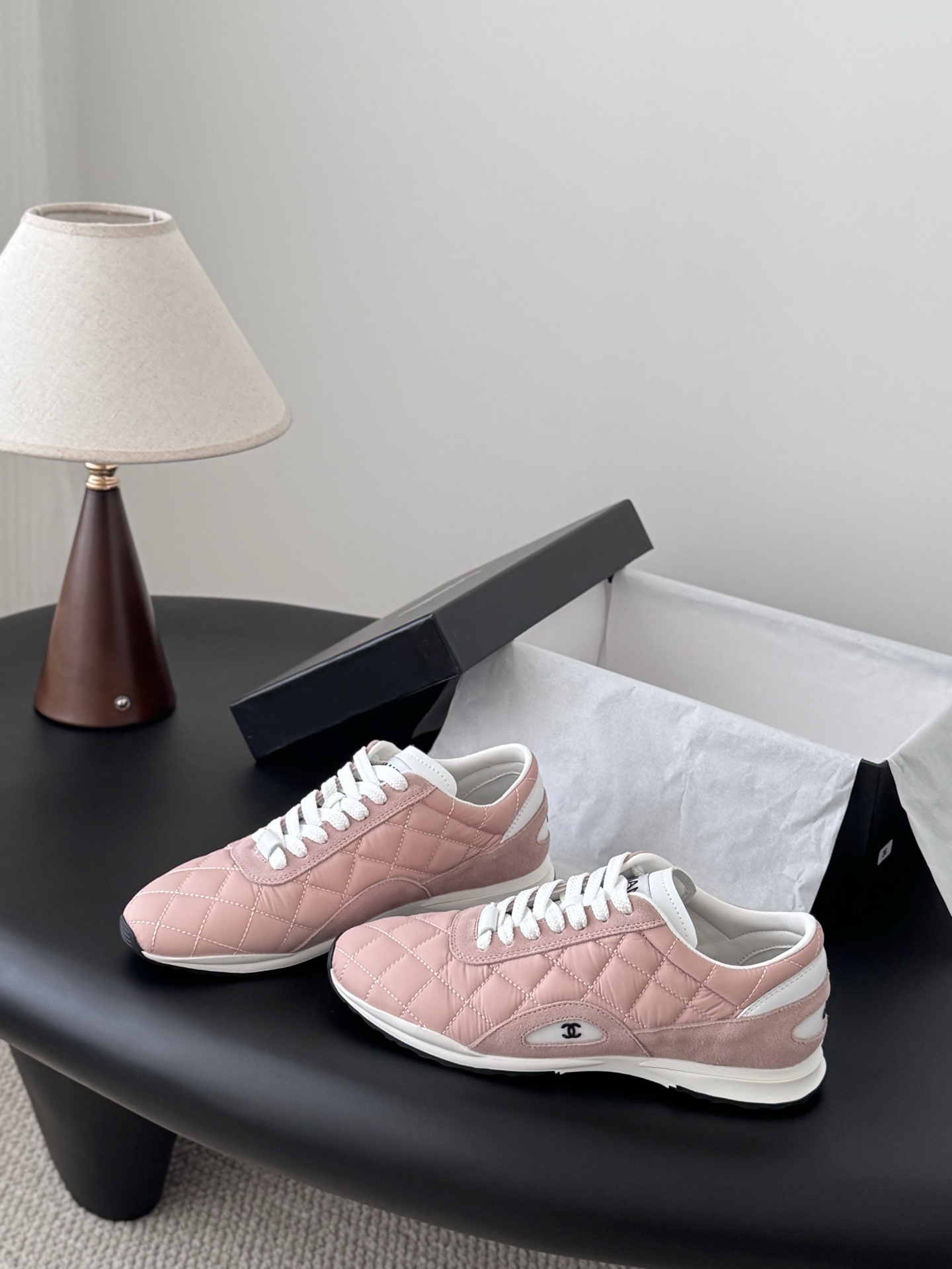 A pair of luxury pink quilted Chanel sneakers with white laces displayed next to their original black designer box. - Hình 2