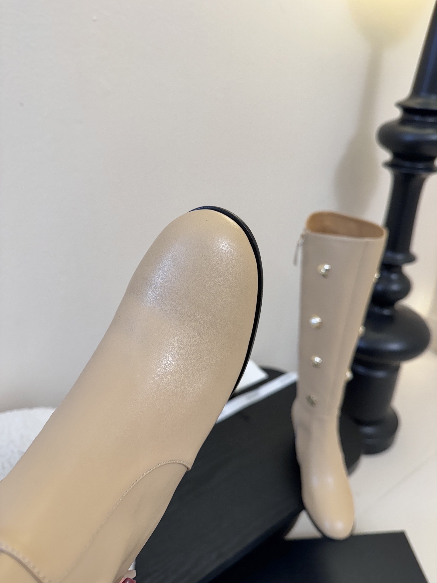 Luxury Chanel beige leather knee-high boots decorated with gold CC logos, pearls, and flower charms on a black display stand. - Hình 6