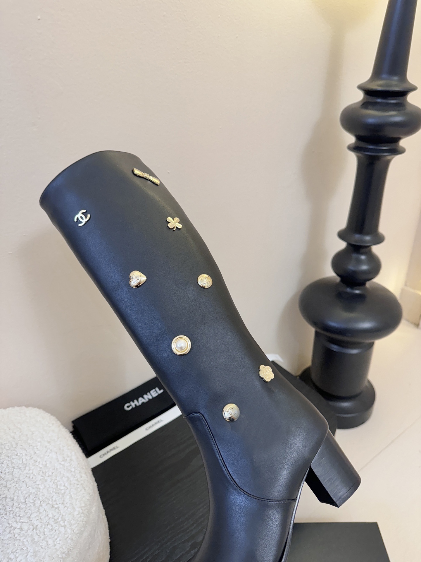Pair of Chanel black leather knee-high boots decorated with gold CC logos, pearls, and heart charms on a black display. - Hình 8