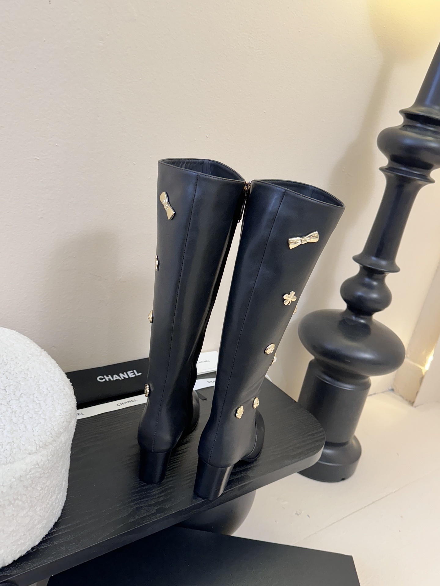 Pair of Chanel black leather knee-high boots decorated with gold CC logos, pearls, and heart charms on a black display. - Hình 7