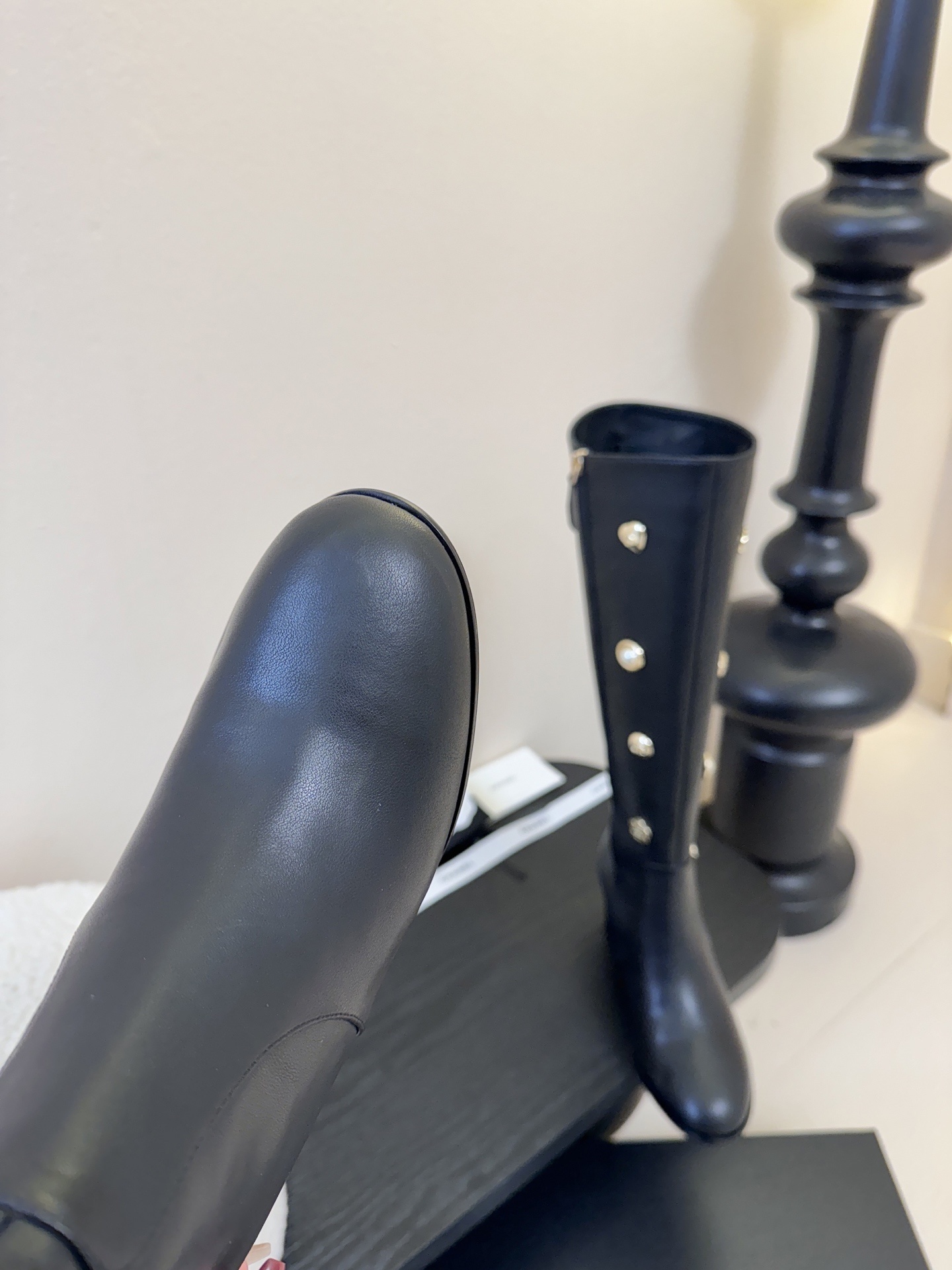 Pair of Chanel black leather knee-high boots decorated with gold CC logos, pearls, and heart charms on a black display. - Hình 6