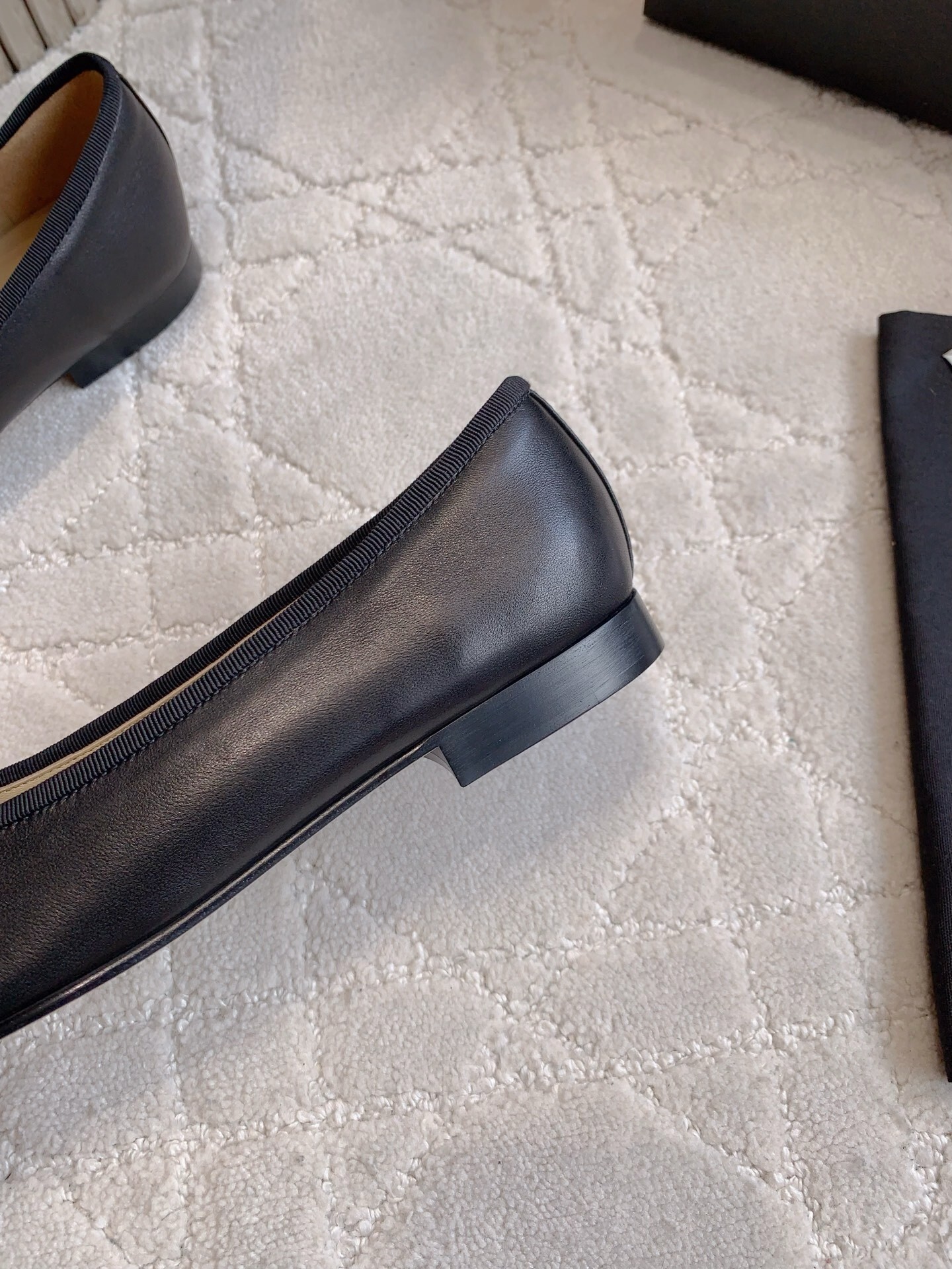 A pair of classic black Chanel lambskin ballerina flats with stitched CC logo and bow detail on a marble surface. - Hình 9