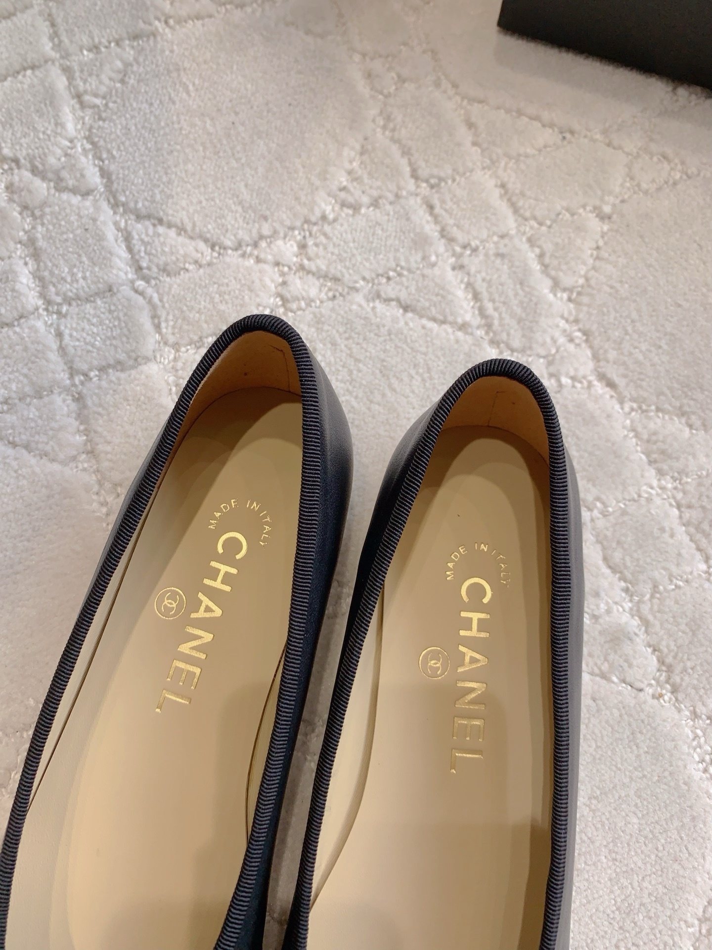 A pair of classic black Chanel lambskin ballerina flats with stitched CC logo and bow detail on a marble surface. - Hình 8