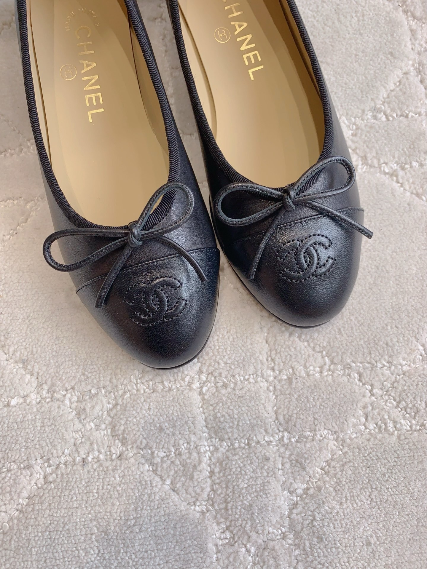 A pair of classic black Chanel lambskin ballerina flats with stitched CC logo and bow detail on a marble surface. - Hình 7