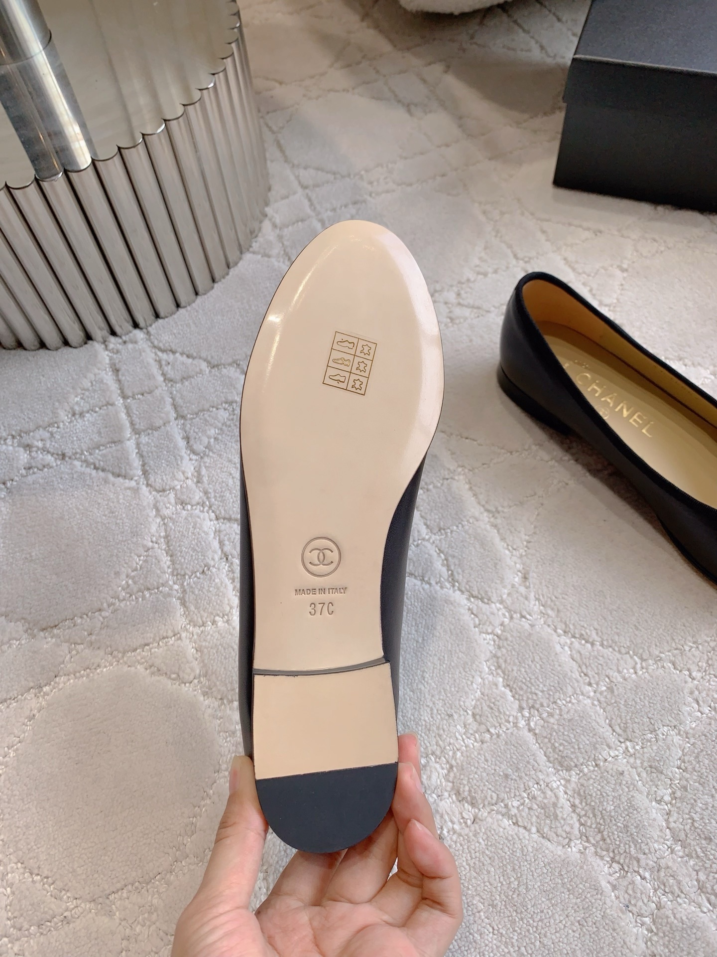 A pair of classic black Chanel lambskin ballerina flats with stitched CC logo and bow detail on a marble surface. - Hình 6