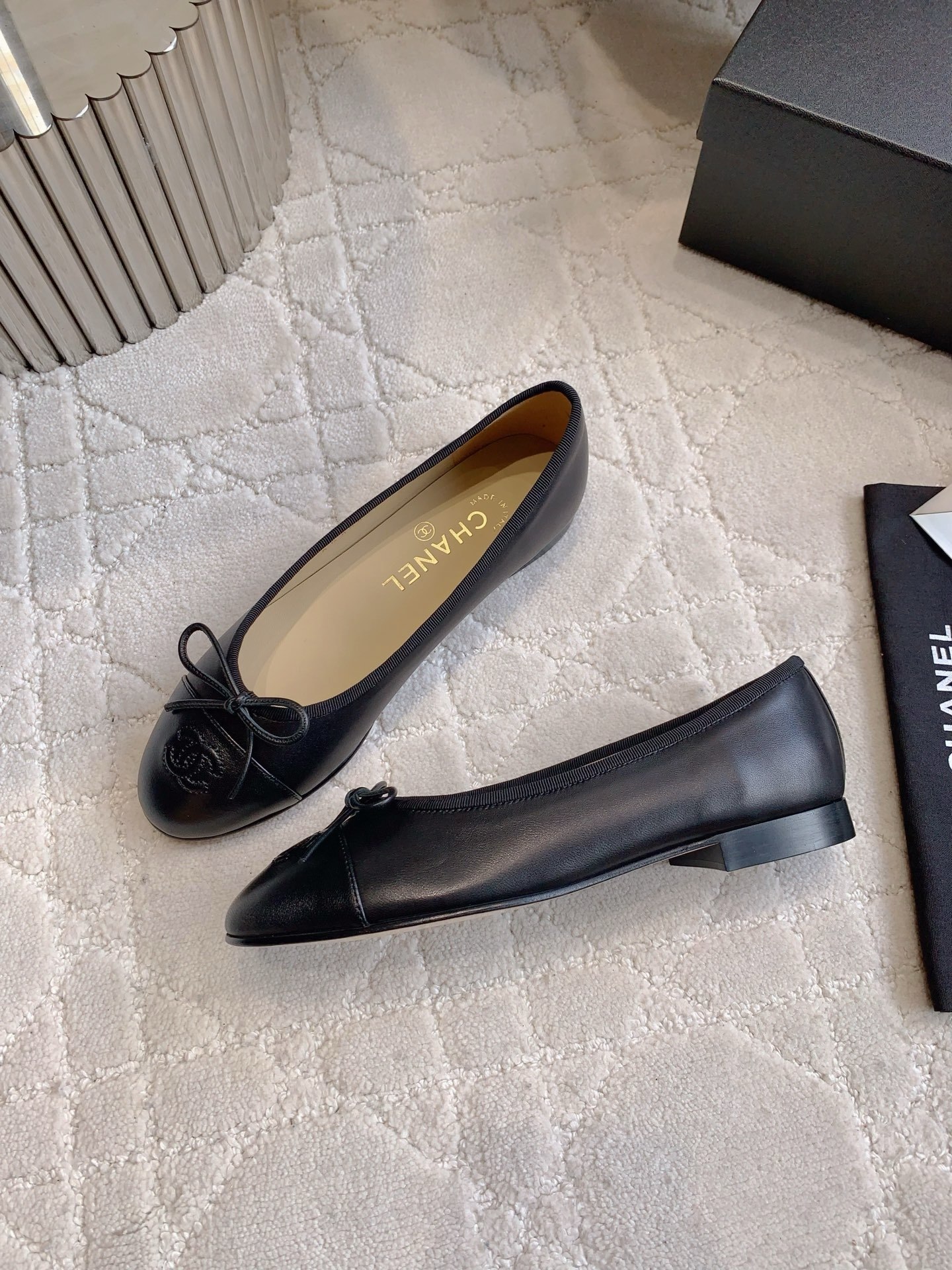 A pair of classic black Chanel lambskin ballerina flats with stitched CC logo and bow detail on a marble surface. - Hình 4