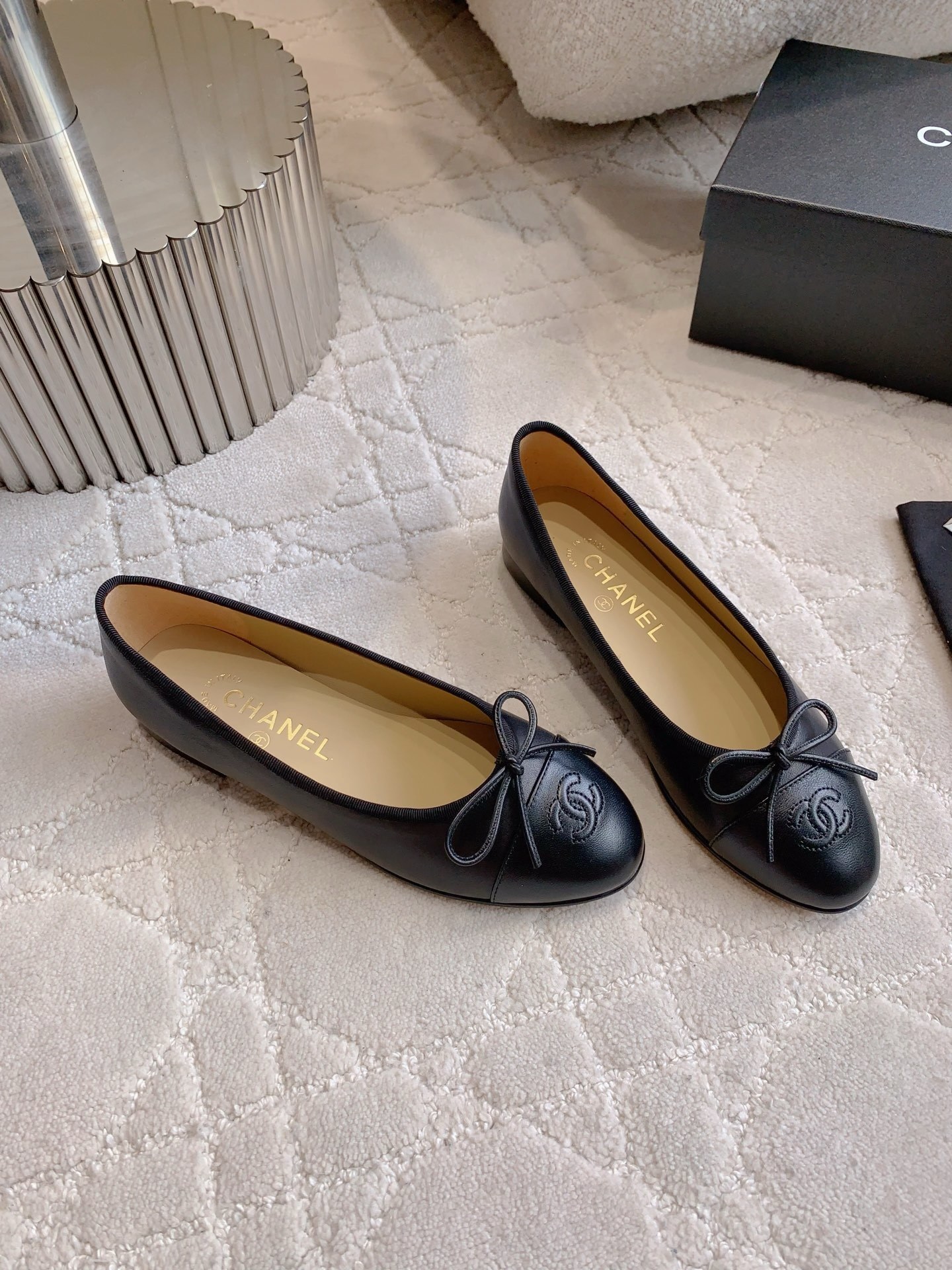 A pair of classic black Chanel lambskin ballerina flats with stitched CC logo and bow detail on a marble surface. - Hình 3