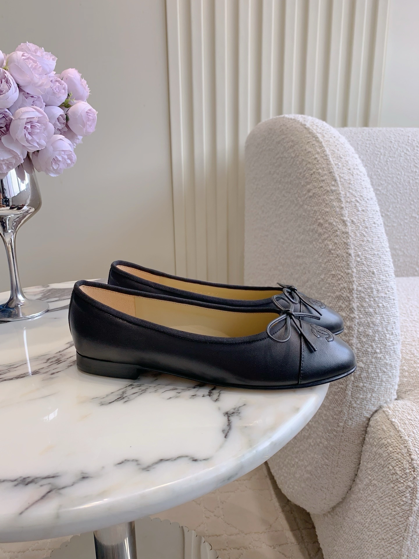 A pair of classic black Chanel lambskin ballerina flats with stitched CC logo and bow detail on a marble surface. - Hình 2