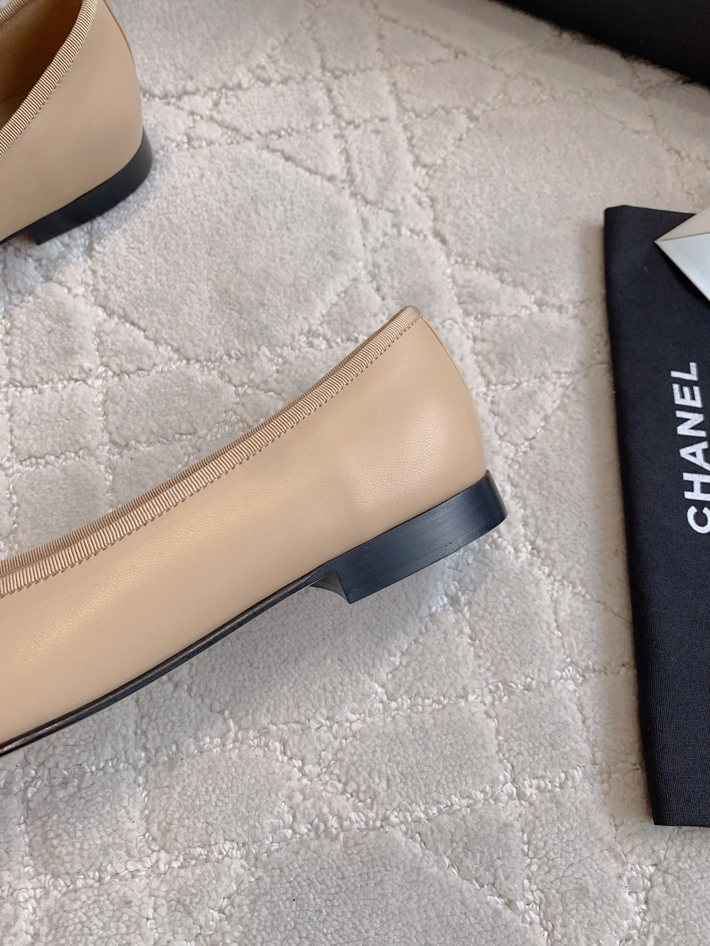Classic Chanel beige lambskin ballerina flats with black toe caps and bow detail displayed on a marble surface. - Hình 9