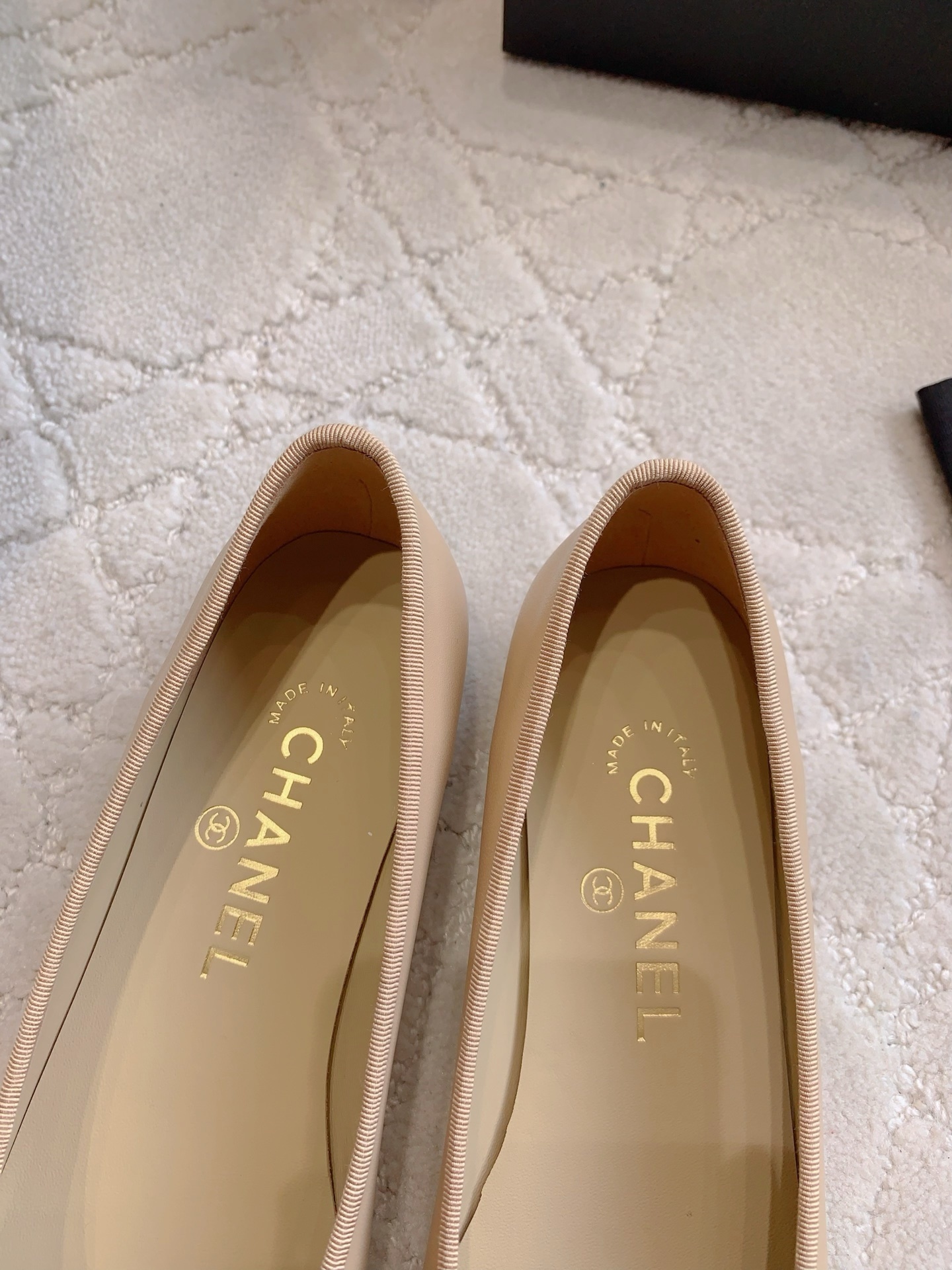 Classic Chanel beige lambskin ballerina flats with black toe caps and bow detail displayed on a marble surface. - Hình 8